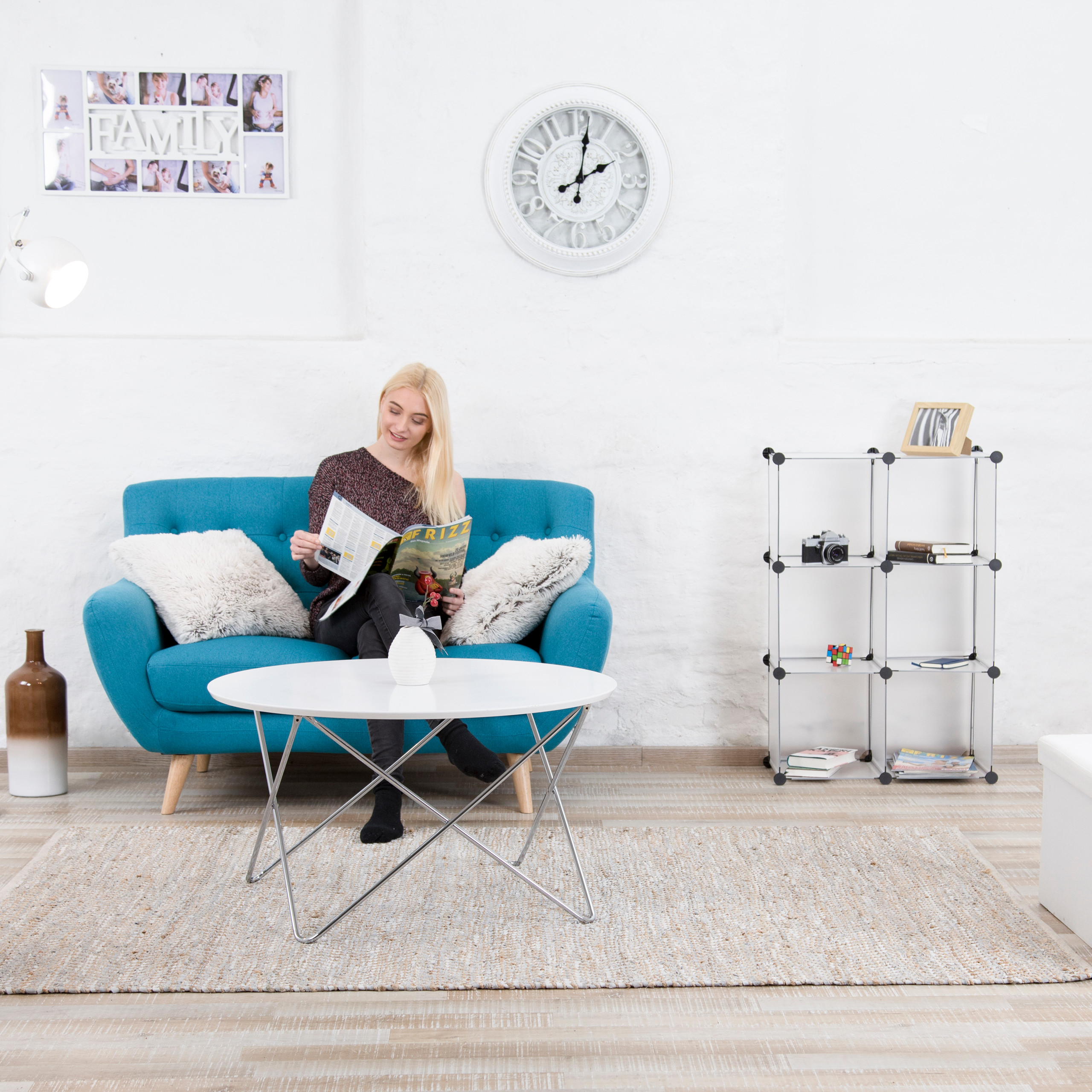 Blonde Frau sitzt auf einem blauen Sofa und liest ein Magazin in einem hellen Wohnzimmer mit weißem Tisch.