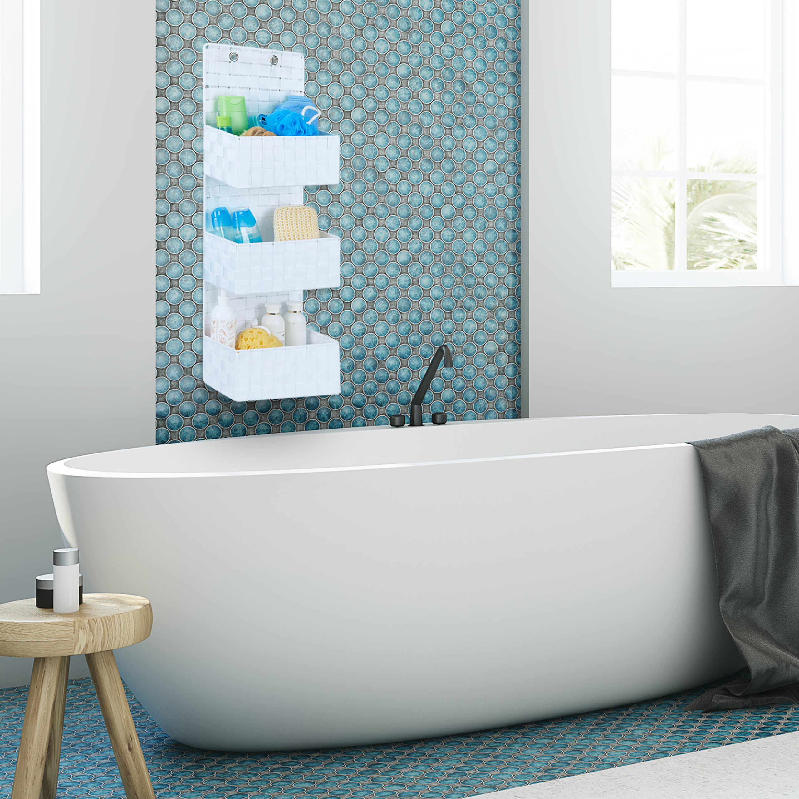 Eine weiße Badewanne mit Hängeorganizer an blauer Fliesenwand, grauem Handtuch und Holzhocker.