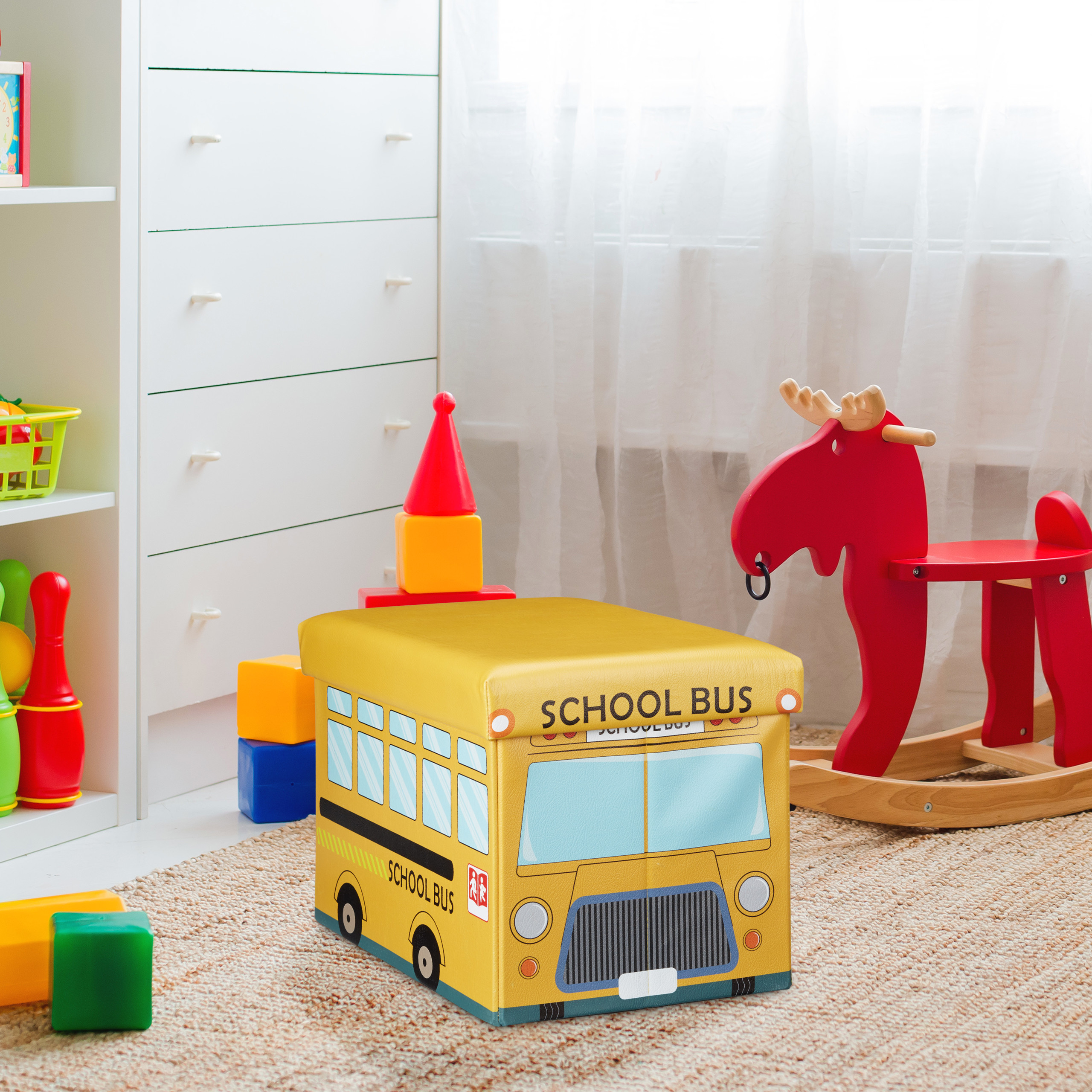 Ein gelber Schulbus-Hocker steht auf einem Teppich in einem Kinderzimmer neben einem roten Holz-Elch und Spielzeug.