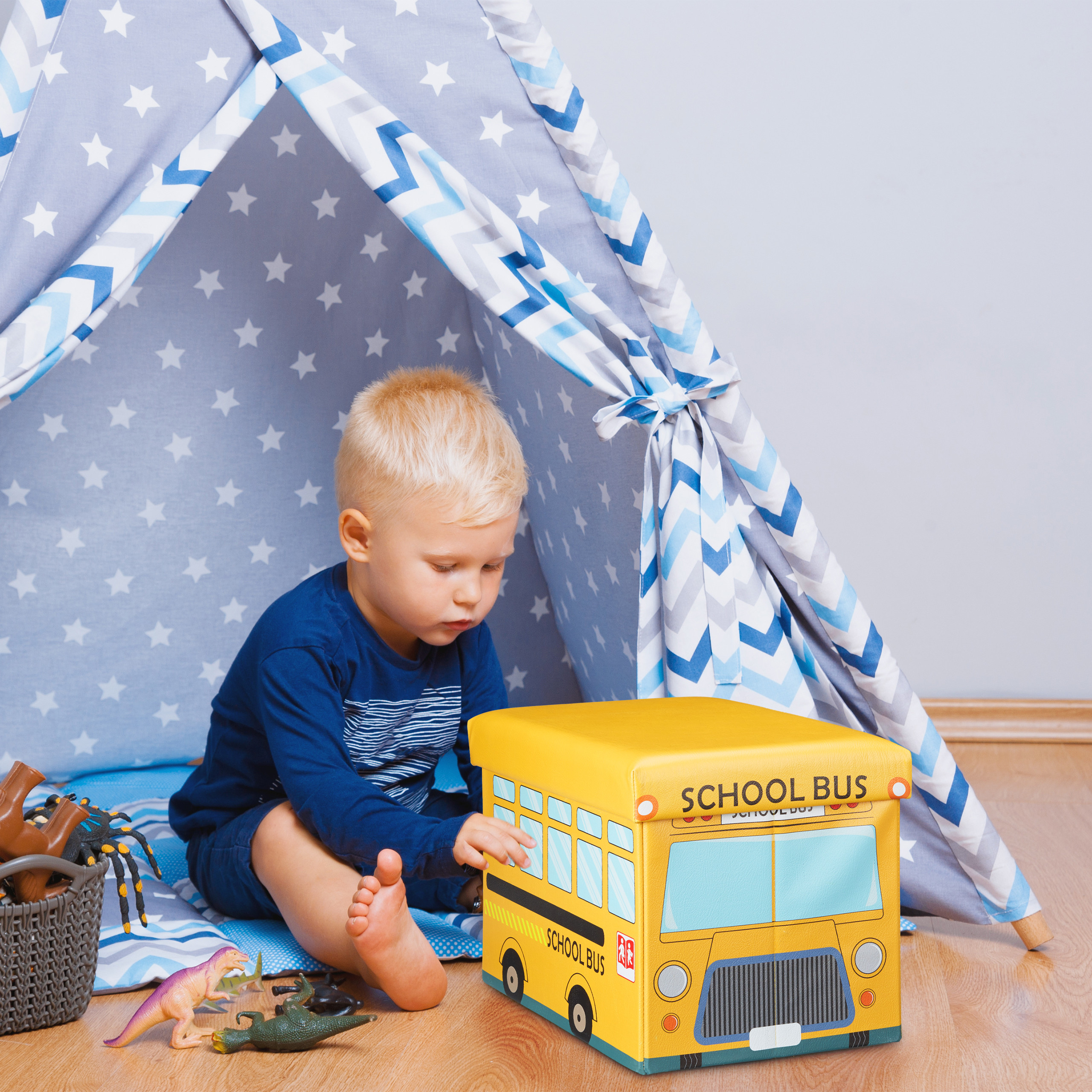 Kleiner Junge im blauen Shirt sitzt in einem grauen Sternezelt neben einer gelben Schulbus-Spielzeugkiste.