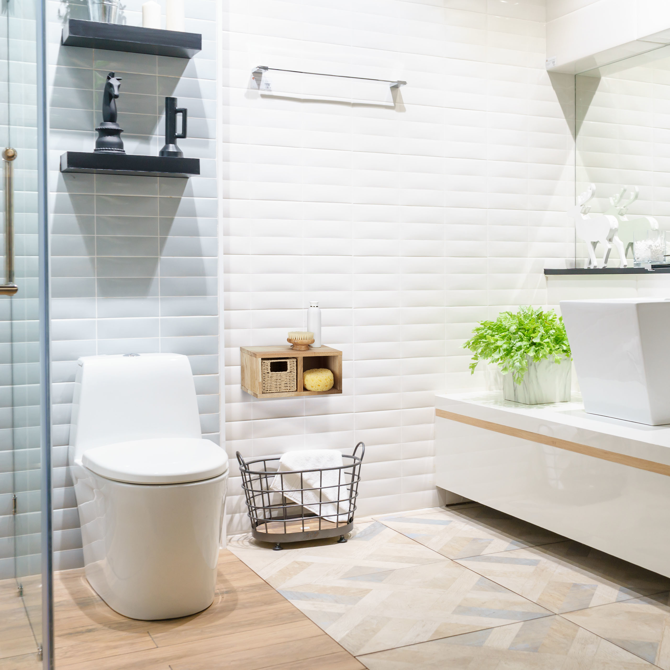 Moderne Badezimmereinrichtung mit weißen Fliesen, schwarzer Toilette, Waschbecken, Pflanzen und Regalen.