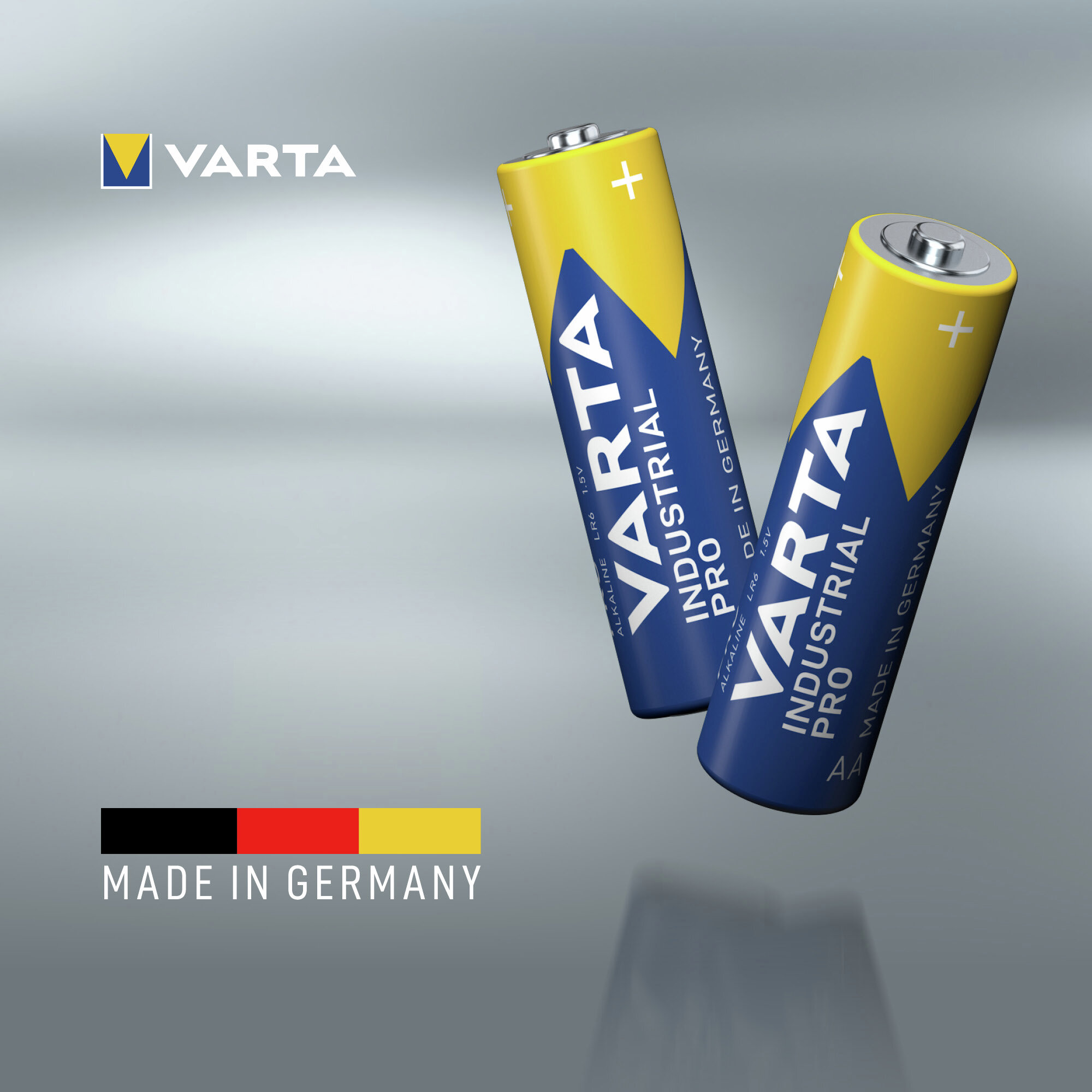 Zwei gelb-blaue Varta Industrial Pro AA-Batterien schweben vor einem silbernen Hintergrund mit dem deutschen Flaggenmotiv.