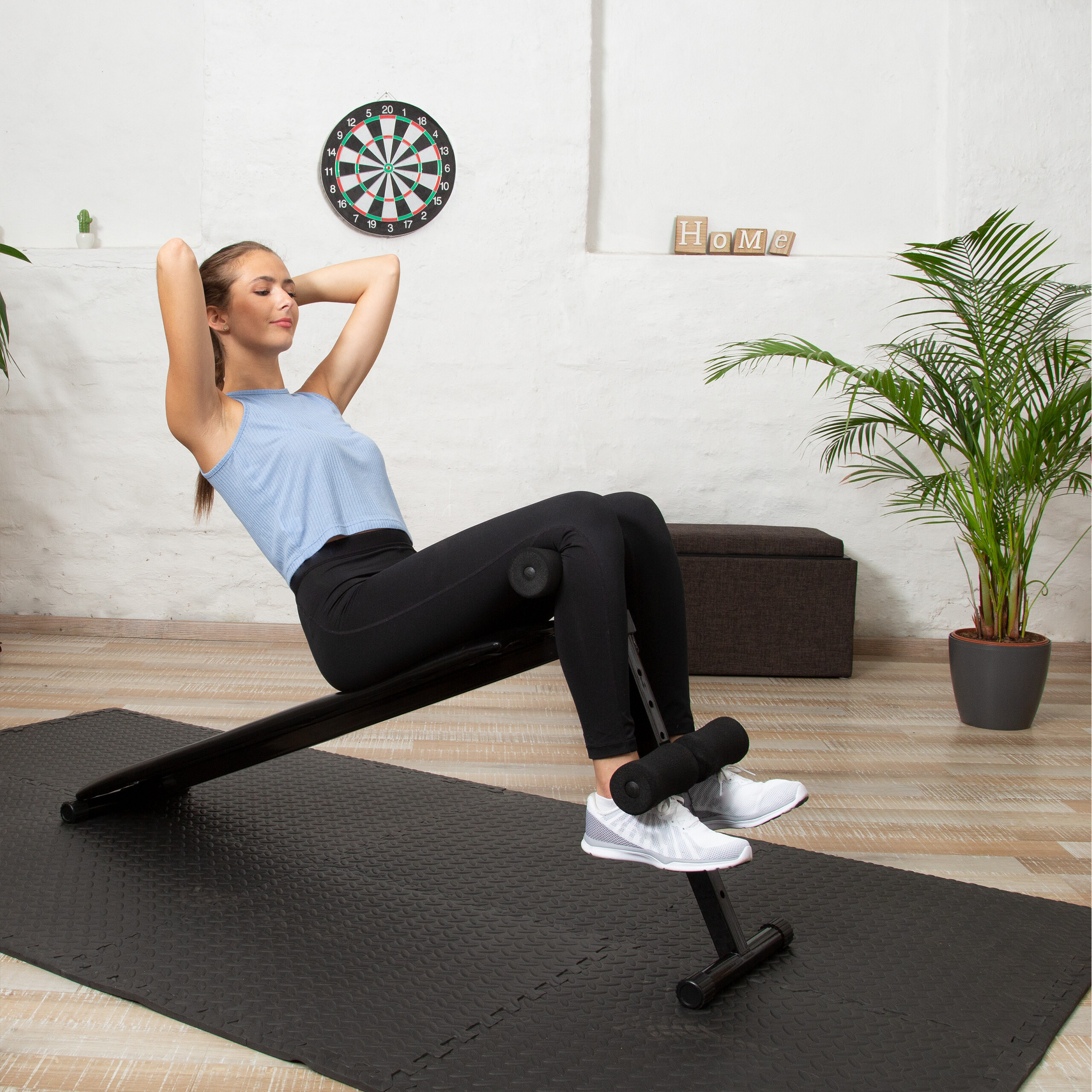 Eine Frau in Sportkleidung macht Sit-ups auf einer Hantelbank in einem hellen Raum.