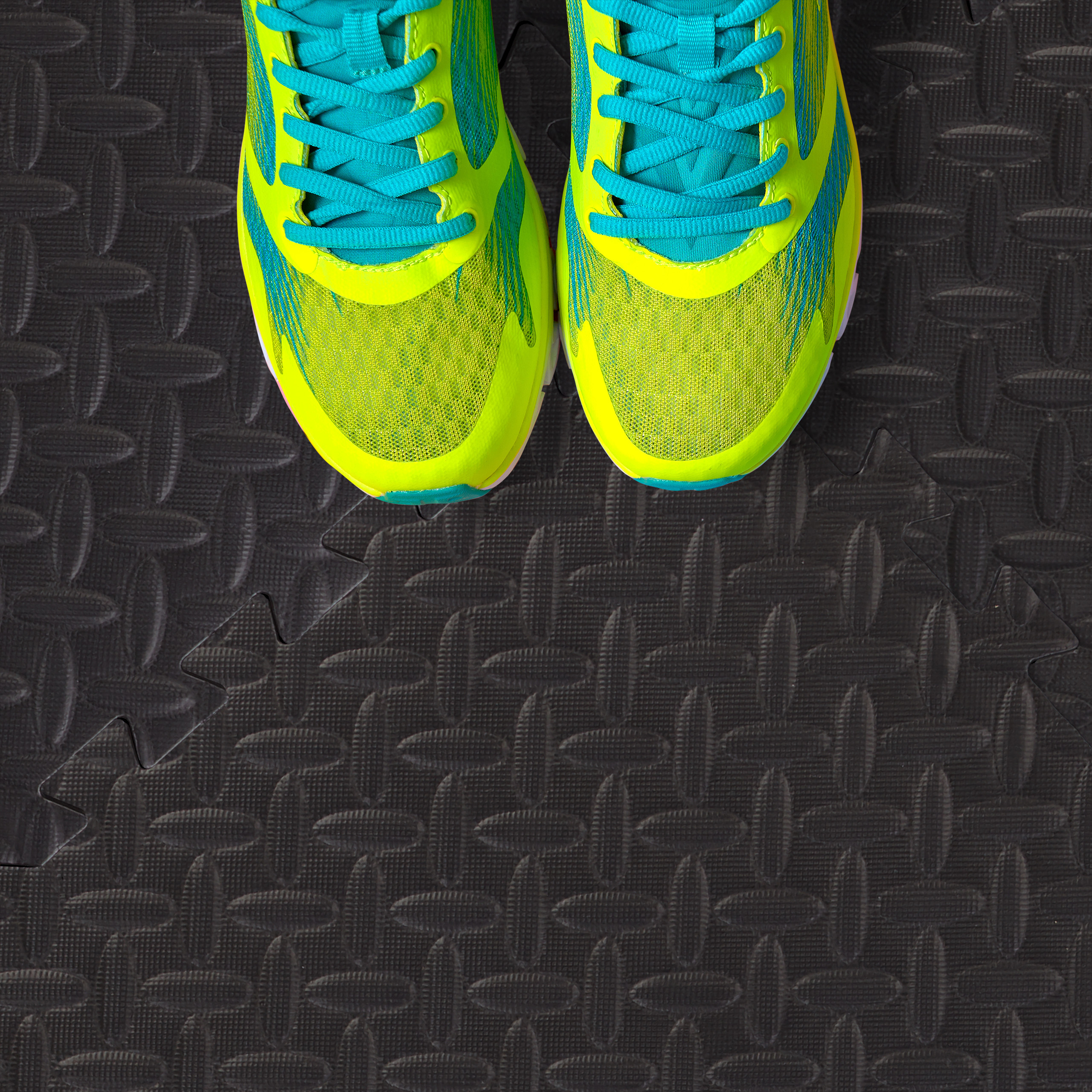 Neongrüne Turnschuhe mit blauen Schnürsenkeln auf einer schwarzen Gummi-Fitnessmatte.