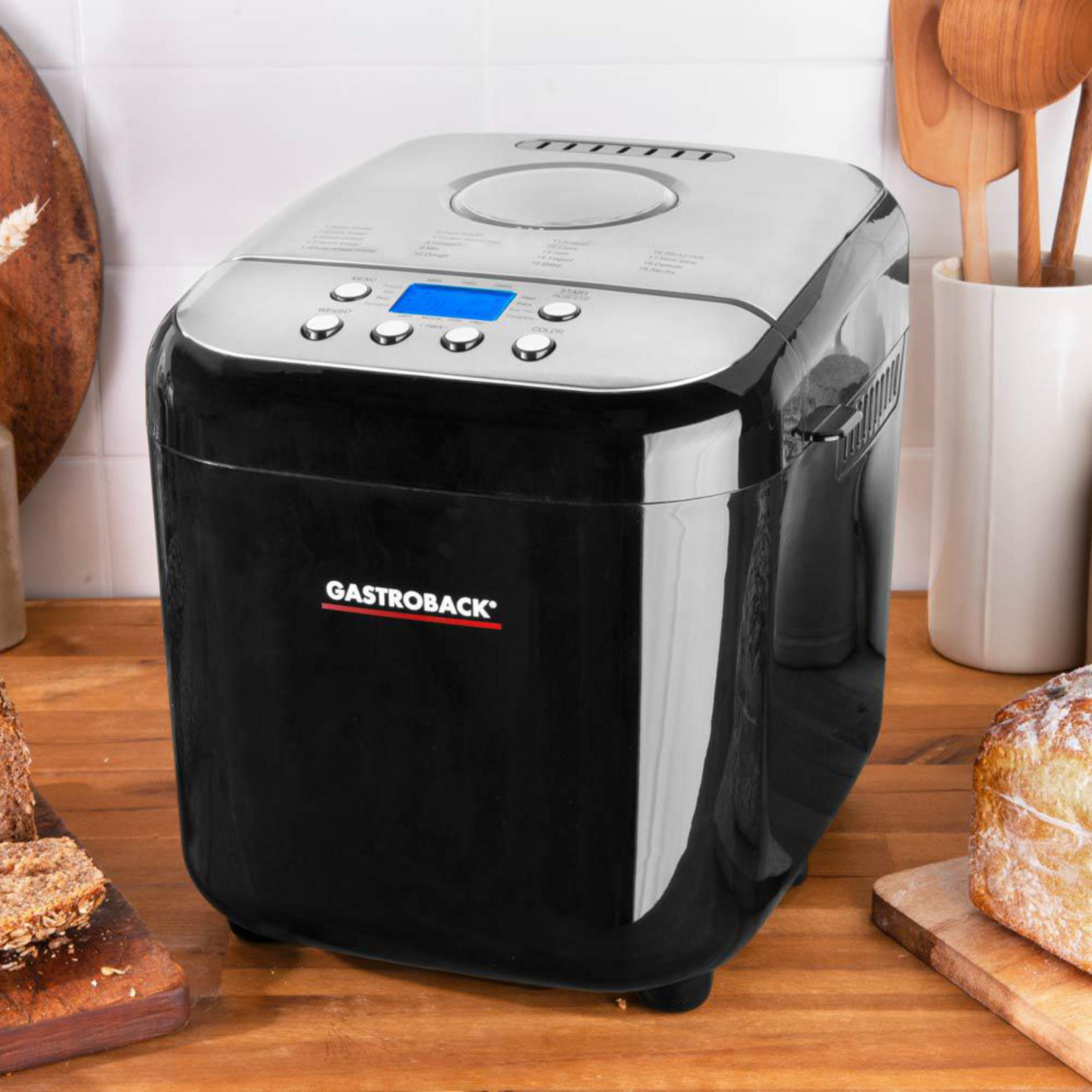 Ein schwarzer Gastroback Brotbackautomat auf einer Holzarbeitsplatte in einer Küche mit Broten.