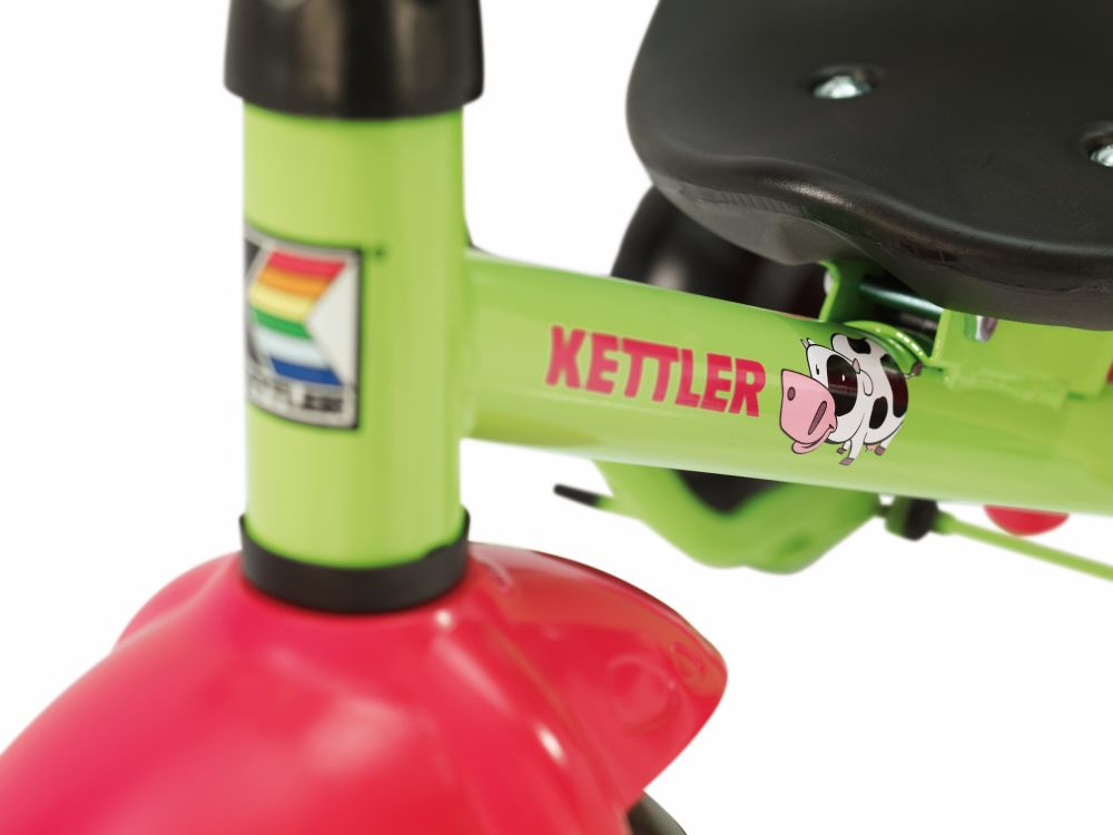 Nahaufnahme eines grünen Kettler-Dreiradrahmens mit pinkfarbenem Schutzblech und Kuhesticker.