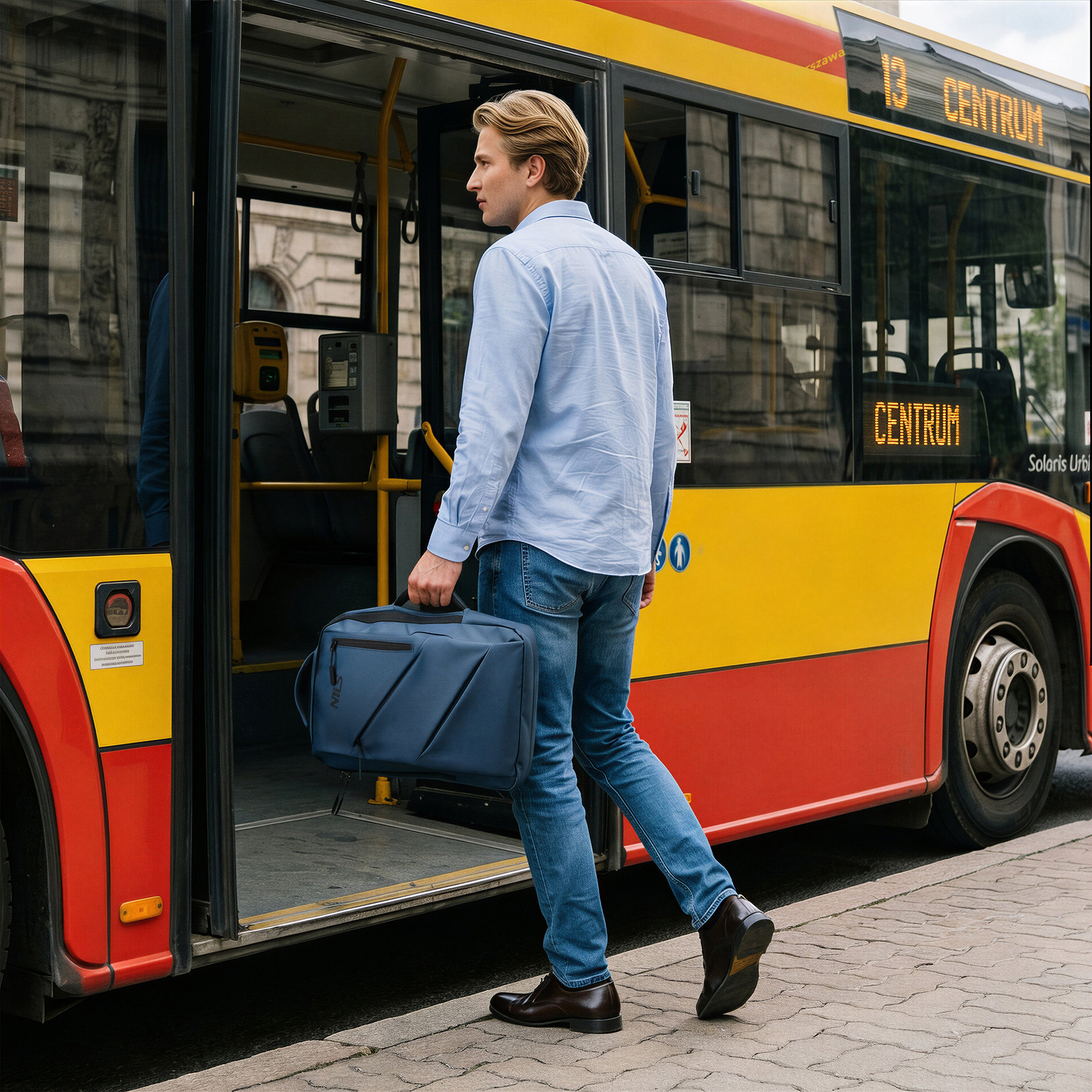 Blondyn z niebieską torbou wsiada do żółto-czerwonego autobusu miejskiego.