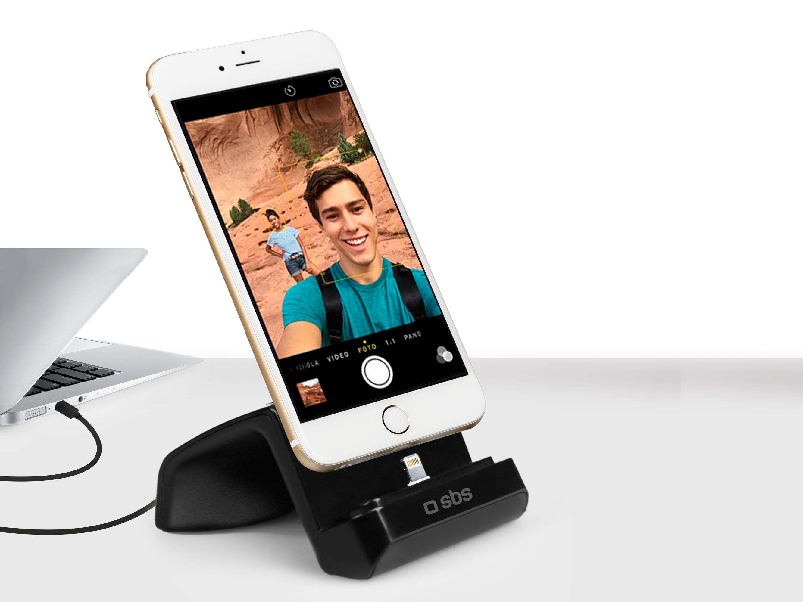 Un smartphone blanco en una base de carga negra, conectado a un portátil gris.