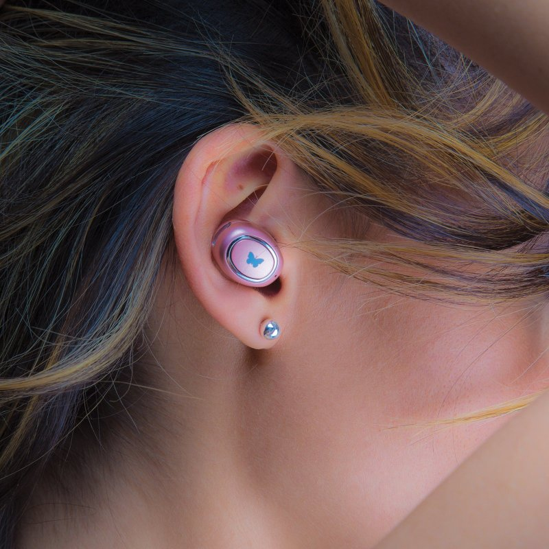 Auricolare wireless rosa con un simbolo di farfalla blu nell'orecchio di una persona con capelli castani.