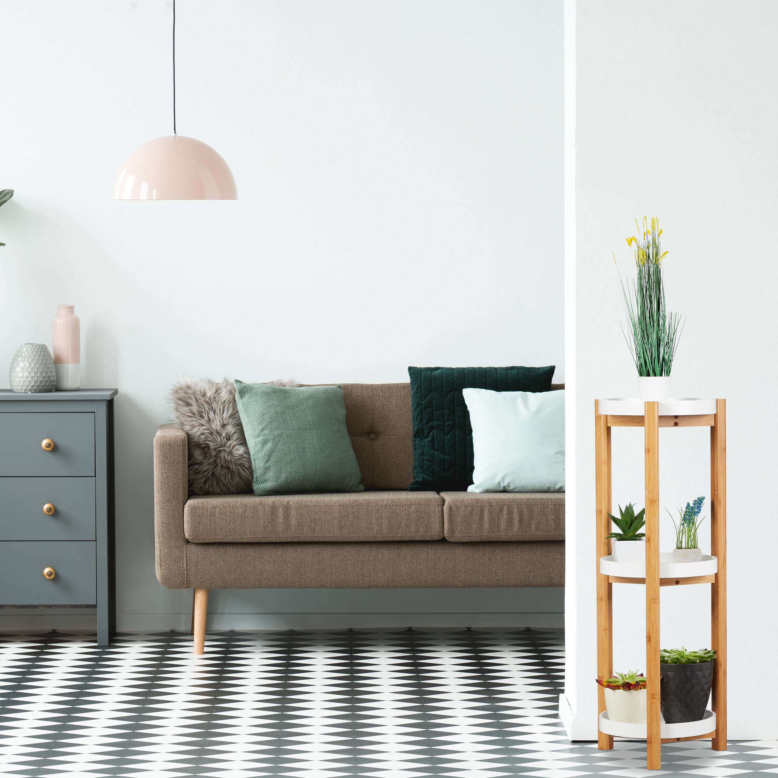 Ein modernes Wohnzimmer mit braunem Sofa, grauer Kommode, rosa Lampe und Pflanzenständer auf schwarz-weißem Karoboden.