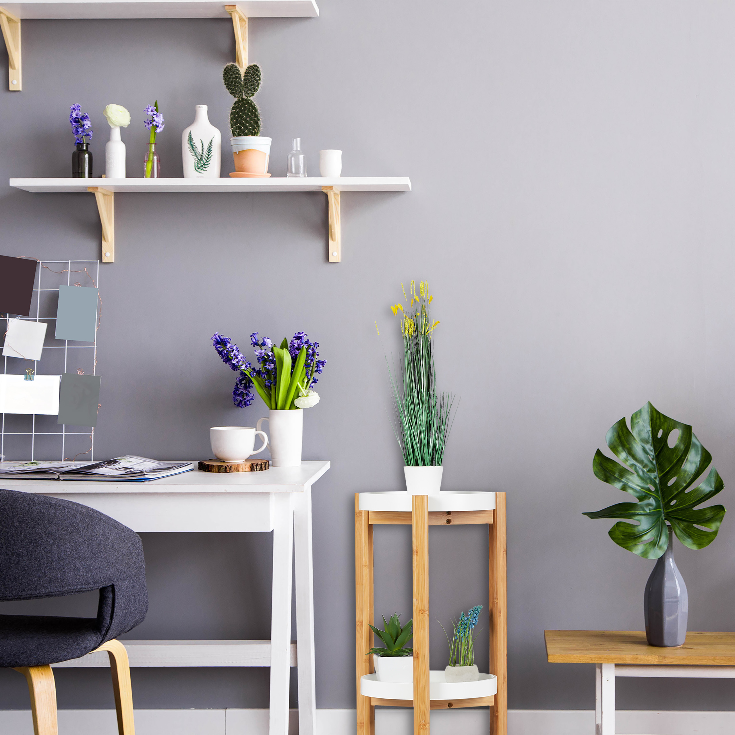 Ein minimalistischer Arbeitsbereich vor grauer Wand mit Regalen, Pflanzen in Vasen, einem Schreibtisch und Holztischen.