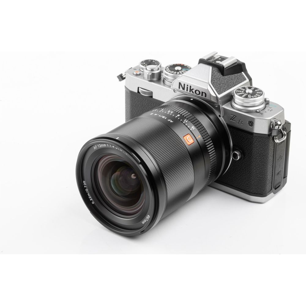 Una fotocamera Nikon Z fc argento e nera con un obiettivo grande su sfondo bianco.