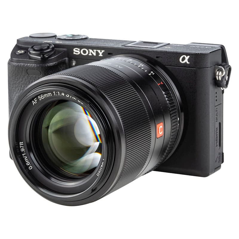 Fotocamera nera Sony con grande obiettivo AF 56mm 1:1.4 su sfondo bianco.