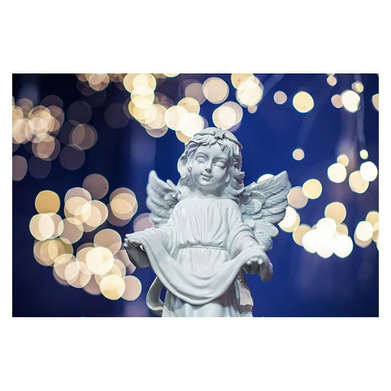 Una statuetta d'angelo bianca su uno sfondo blu sfocato con luci gialle.