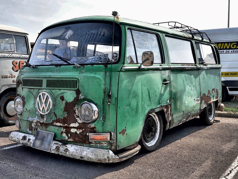 Ein alter, verrosteter grüner VW-Bus parkt auf Asphalt.