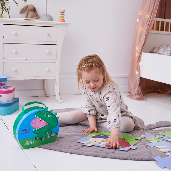 Ein junges Mädchen sitzt auf einer grauen Matte und macht ein Peppa-Wutz-Puzzle auf einem weißen Boden.