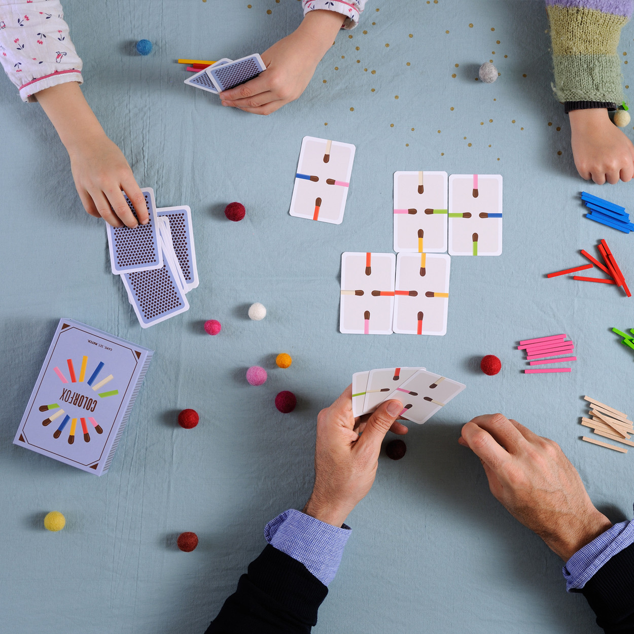 Personen spielen ein Kartenspiel mit bunten Streichholzmustern auf einem blauen Tisch.