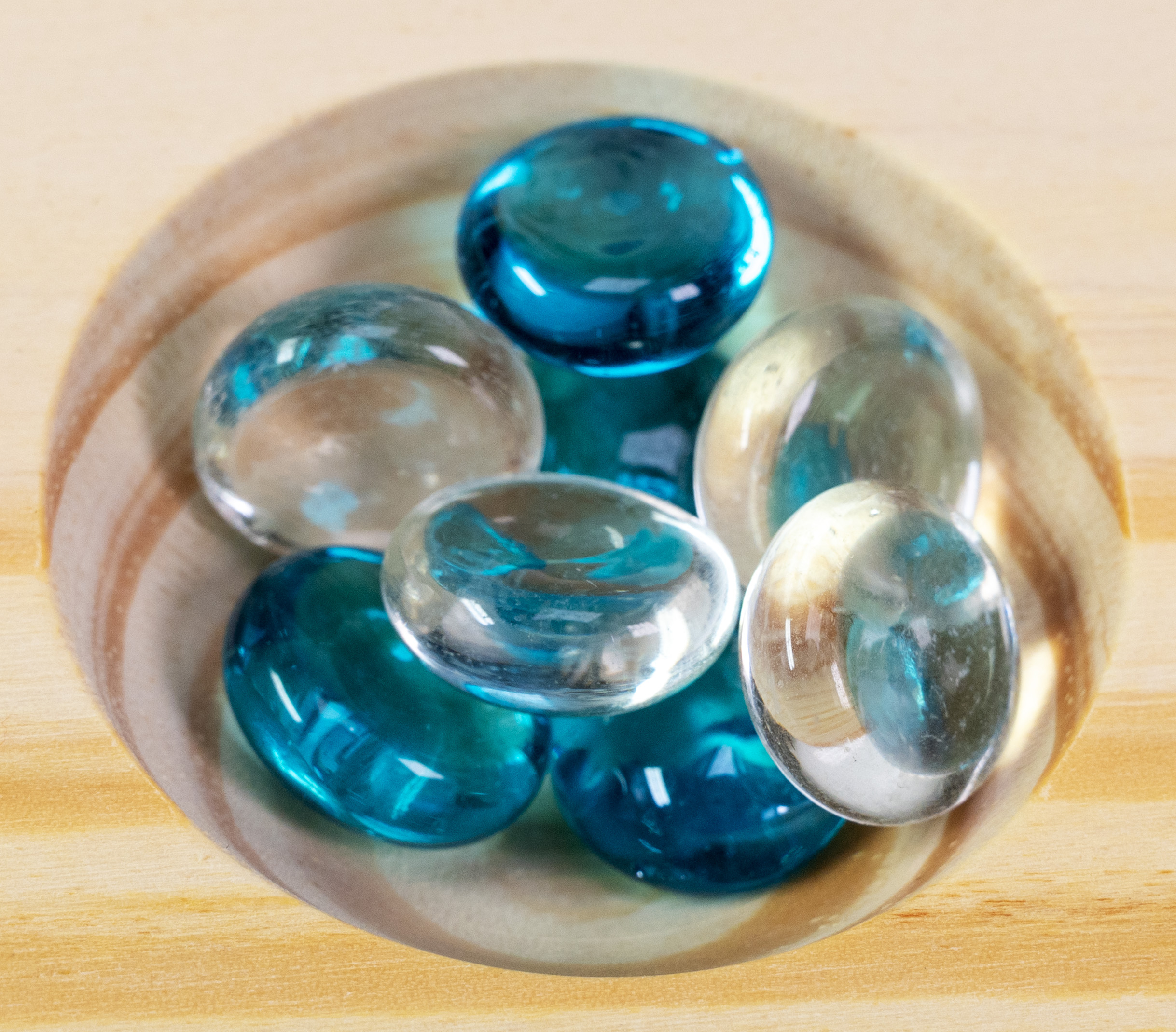 Blaue und transparente Glaskugeln in einer Holzschale.