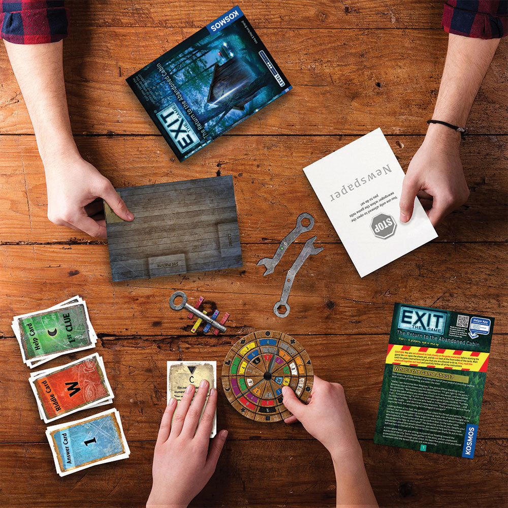 Personen spielen das EXIT-Brettspiel auf einem Holztisch mit Karten, Dekodierscheibe, Schlüsseln und Regelheft.
