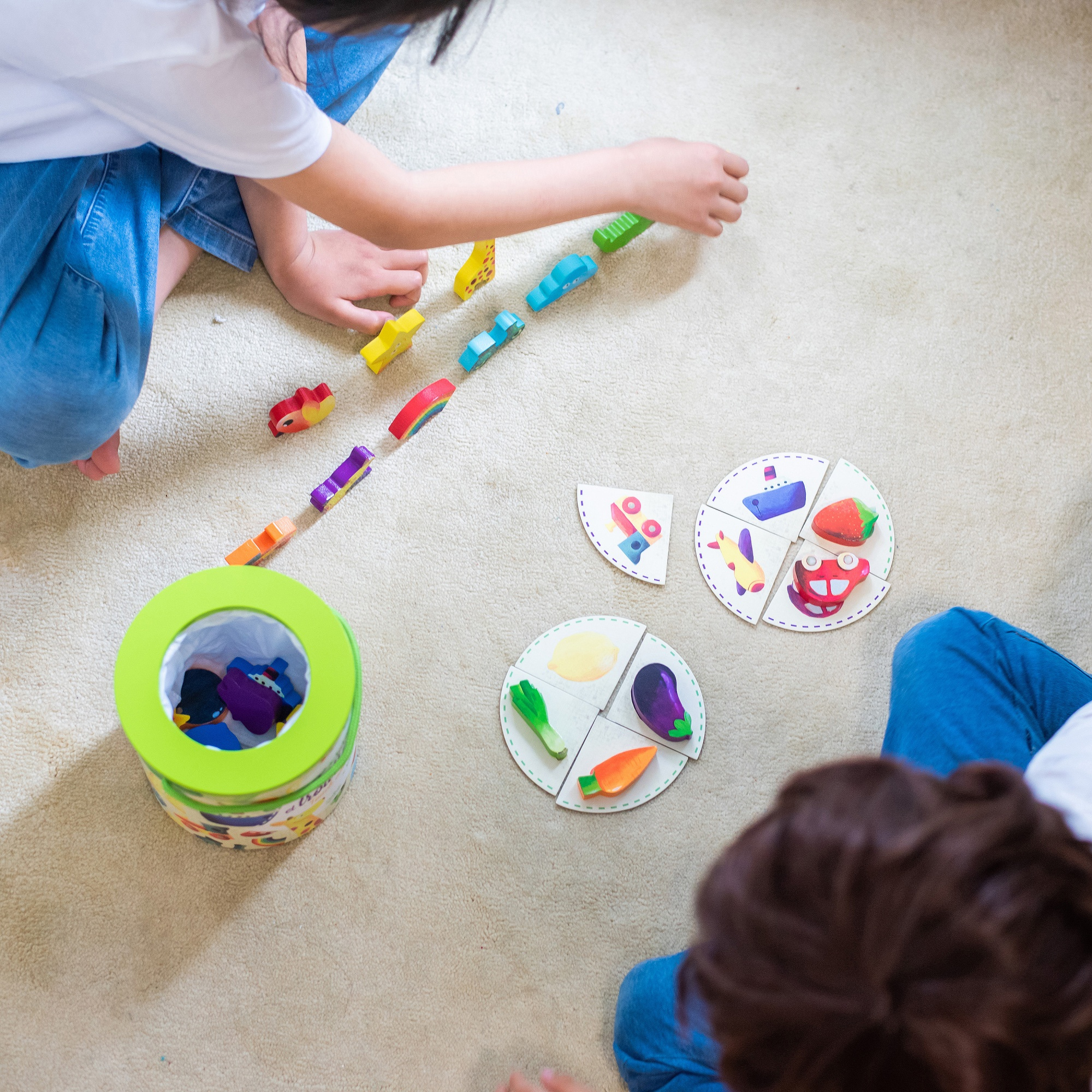 Zwei Kinder sitzen auf einem Teppich und spielen mit Holzspielzeug und Puzzle-Scheiben.