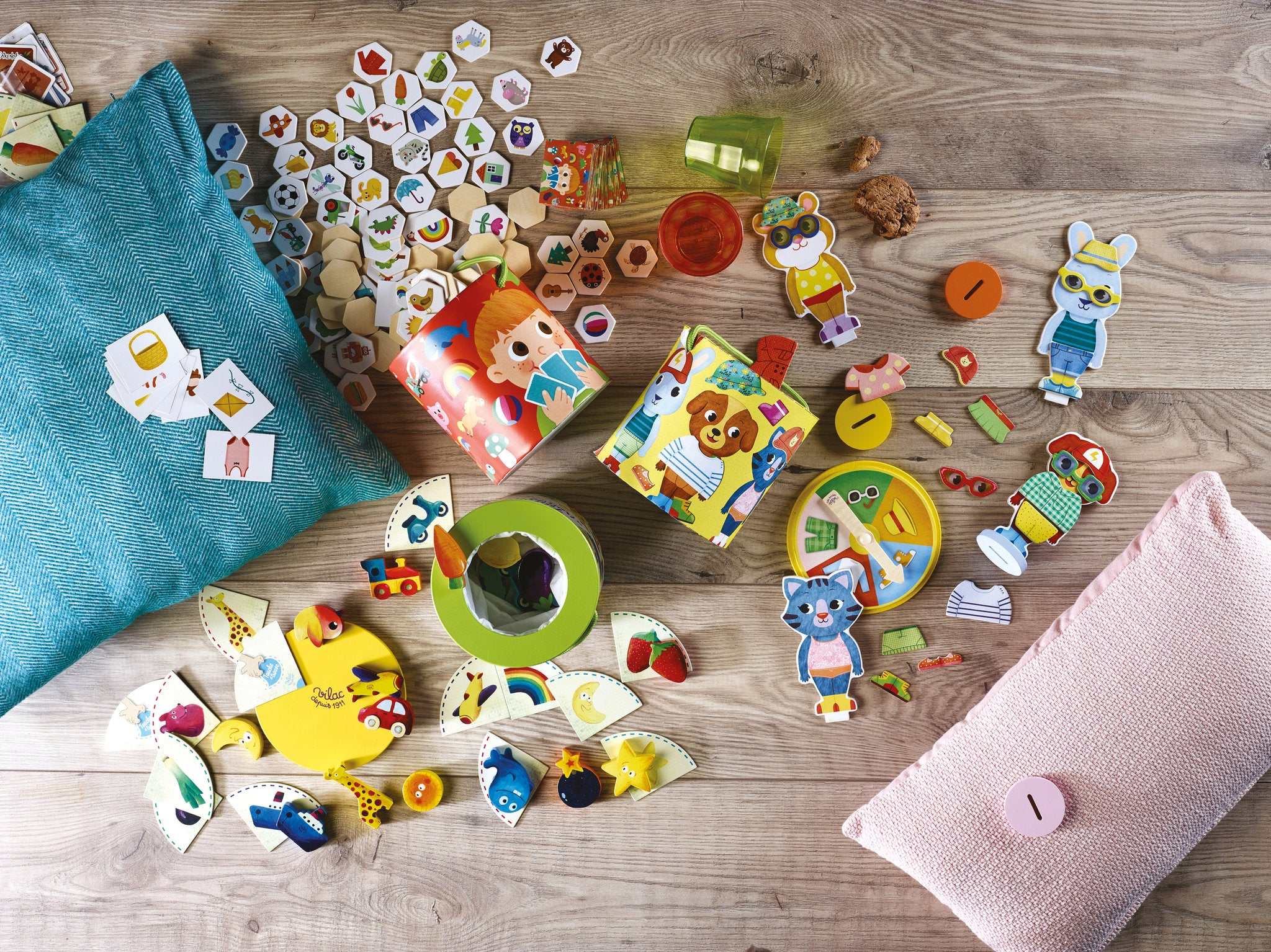 Bunte Holzspielzeuge, Puzzles und Figuren auf Holzboden, flankiert von Kissen.