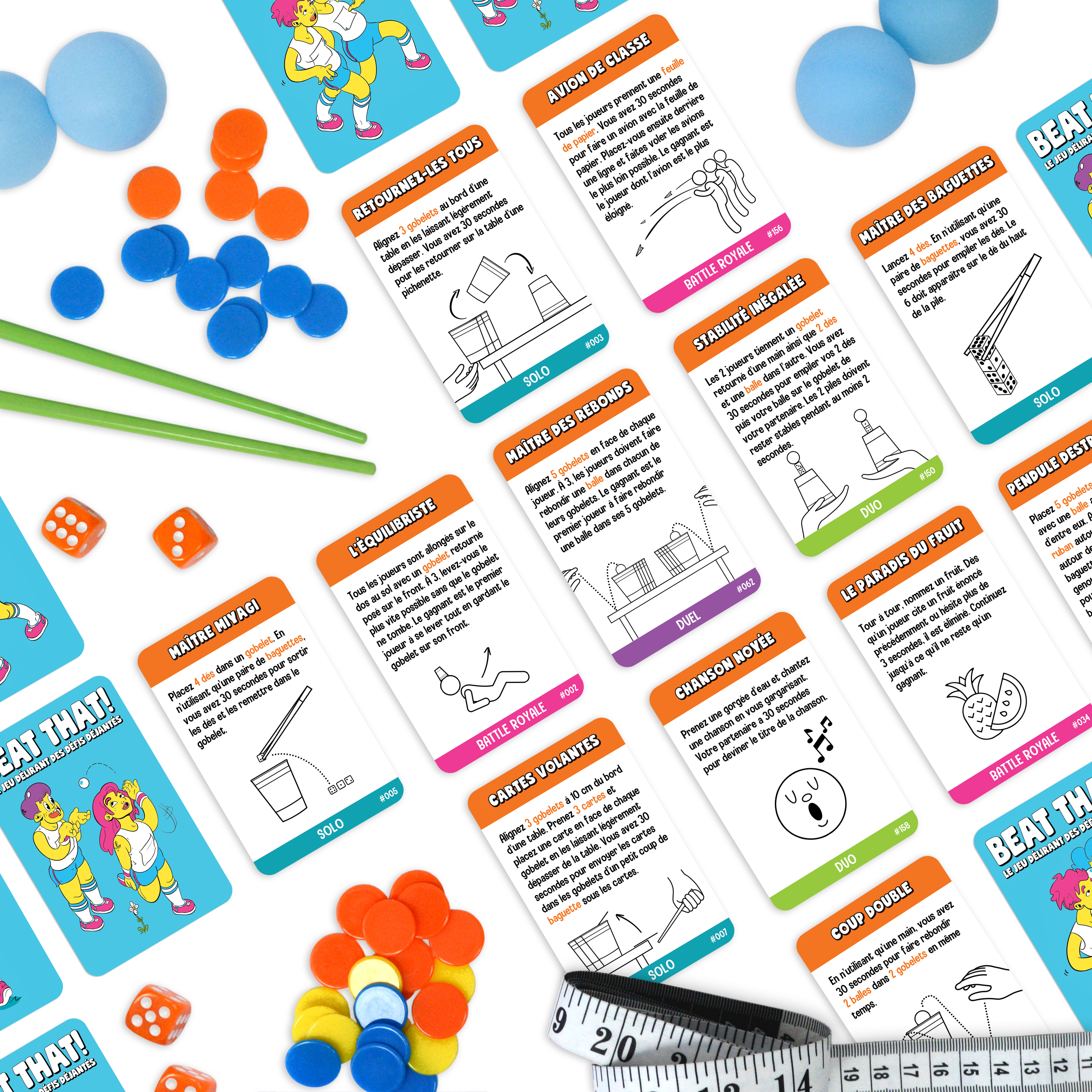 Verschiedene bunte Spielkarten, Würfel, Plastikbecher und Zubehör liegen verteilt auf einer weißen Oberfläche.