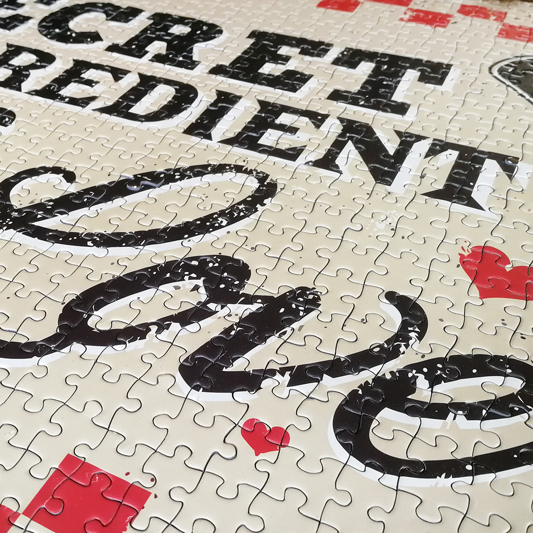 Ein teilweise zusammengesetztes Puzzle mit schwarzer Schrift und roten Herzen auf hellem Hintergrund.