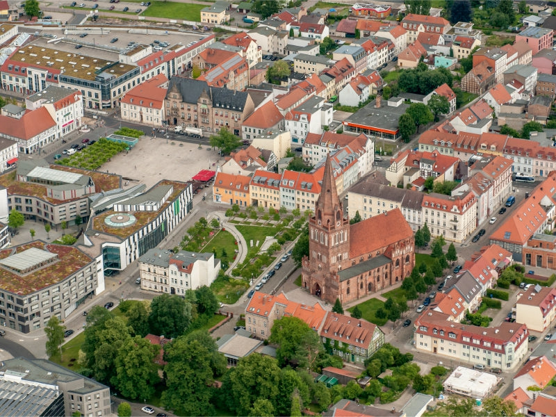 Luftaufnahme einer Stadt mit roter Backsteinkirche, zentralem Platz und vielen Gebäuden mit roten Dächern.