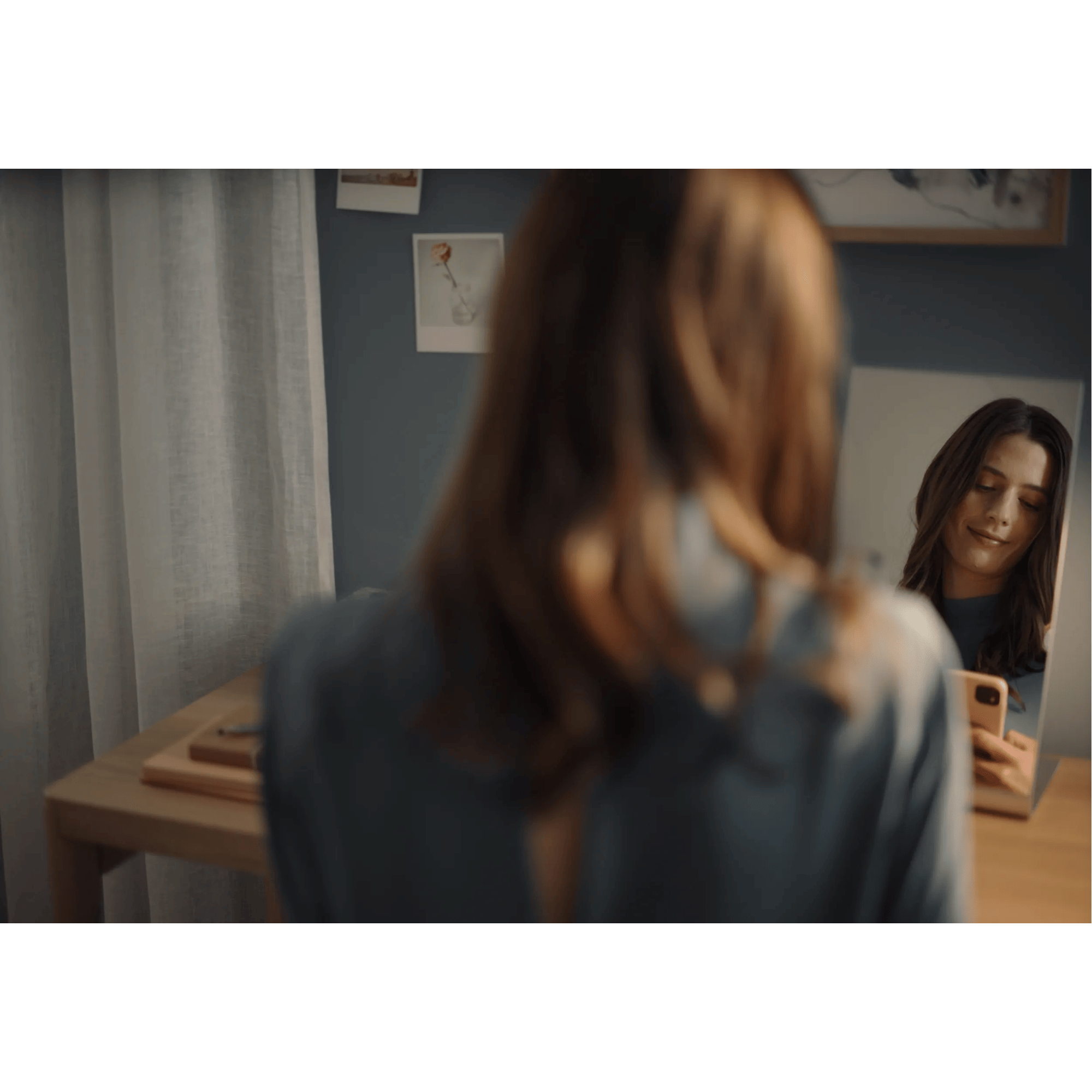 Una mujer está sentada en un escritorio de espaldas, sonriendo mientras se mira en un espejo.