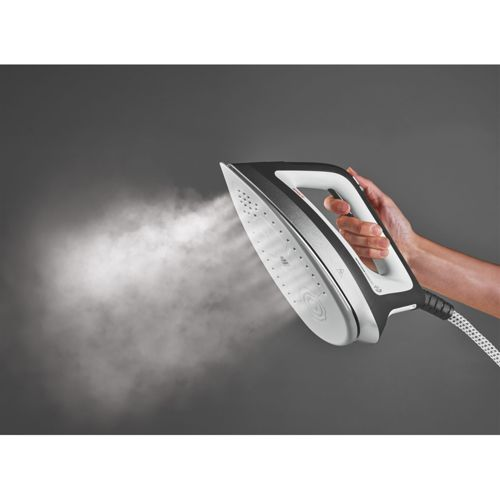 Una mano sostiene una plancha de vapor moderna en blanco y negro, liberando vapor sobre un fondo oscuro.