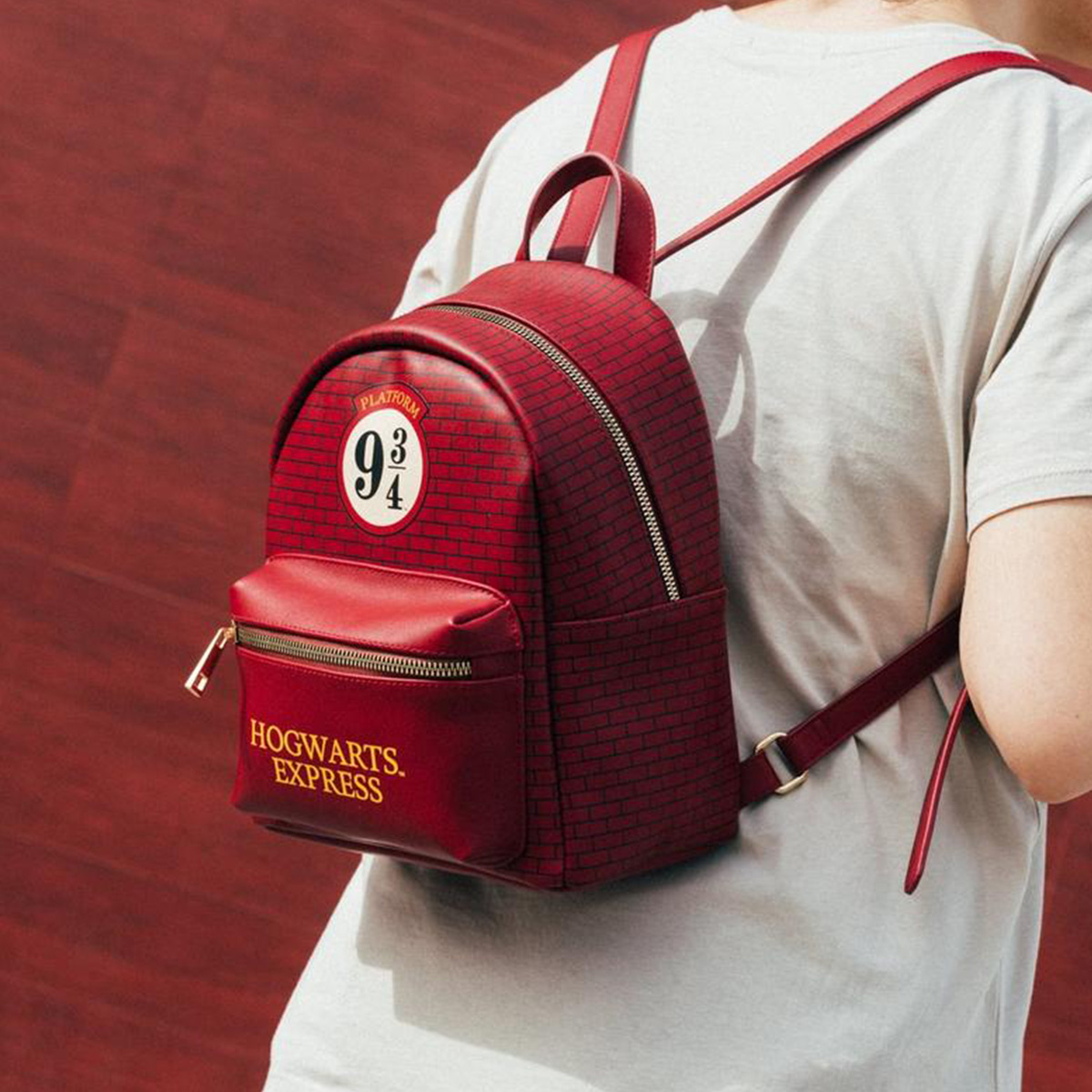 Una persona lleva una mochila roja de Harry Potter frente a una pared de ladrillo.