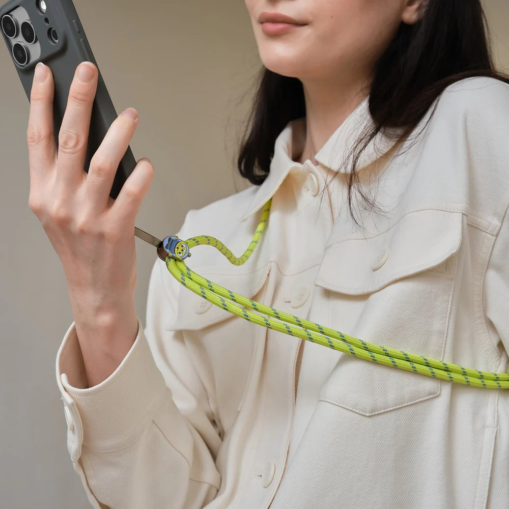 Kobieta w białej kurtce trzyma smartfon przymocowany do neonowozielonej smyczy.