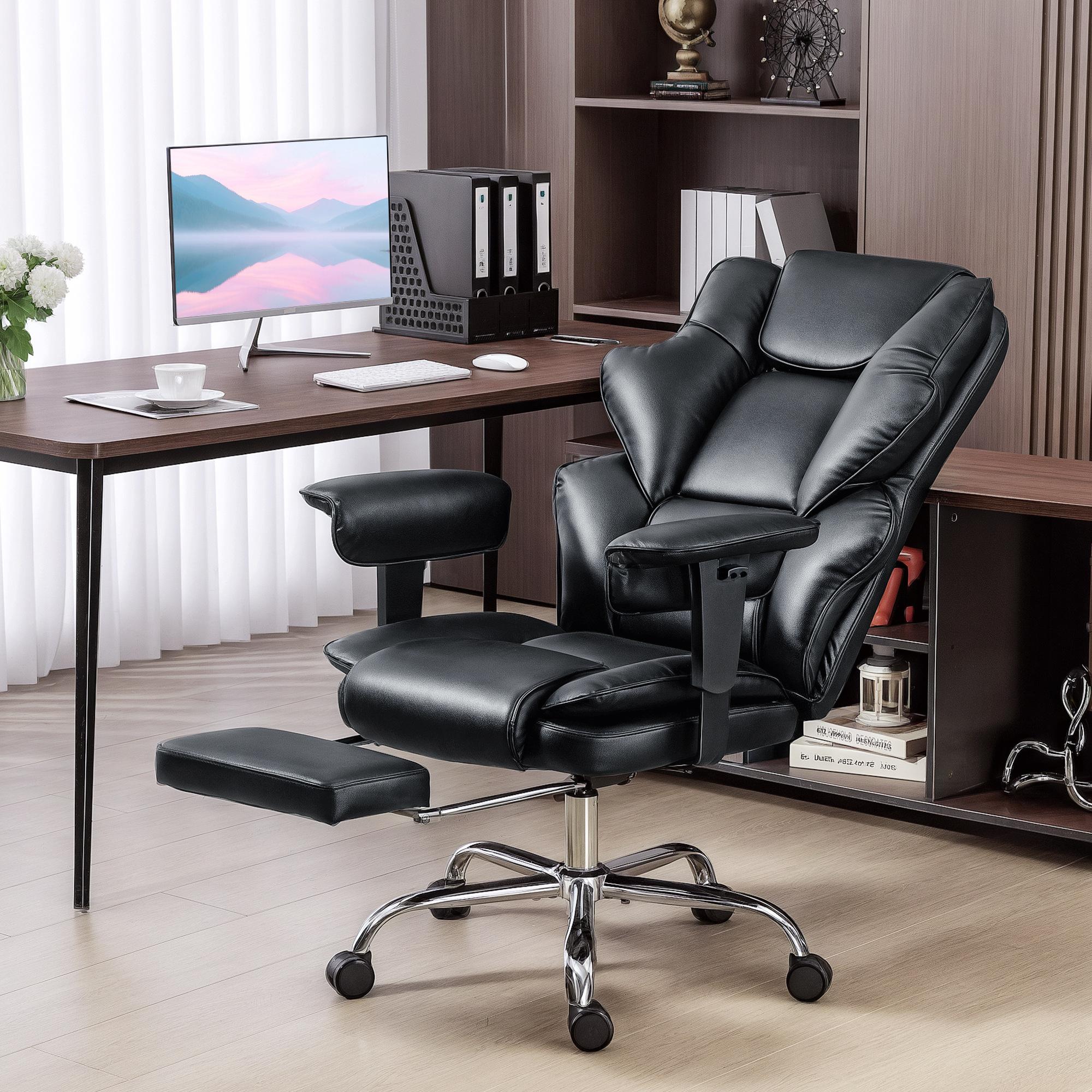 Una sedia da ufficio in pelle nera con poggiapiedi estraibile si trova davanti a una scrivania in legno scuro con monitor in una stanza luminosa.