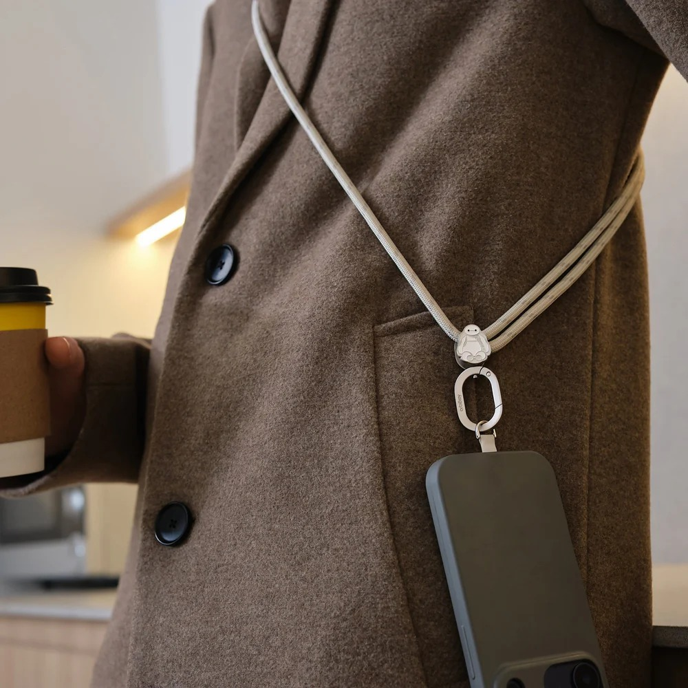Osoba w brązowym płaszczu ma smartfon na długiej smyczy zawieszonej na szyi.
