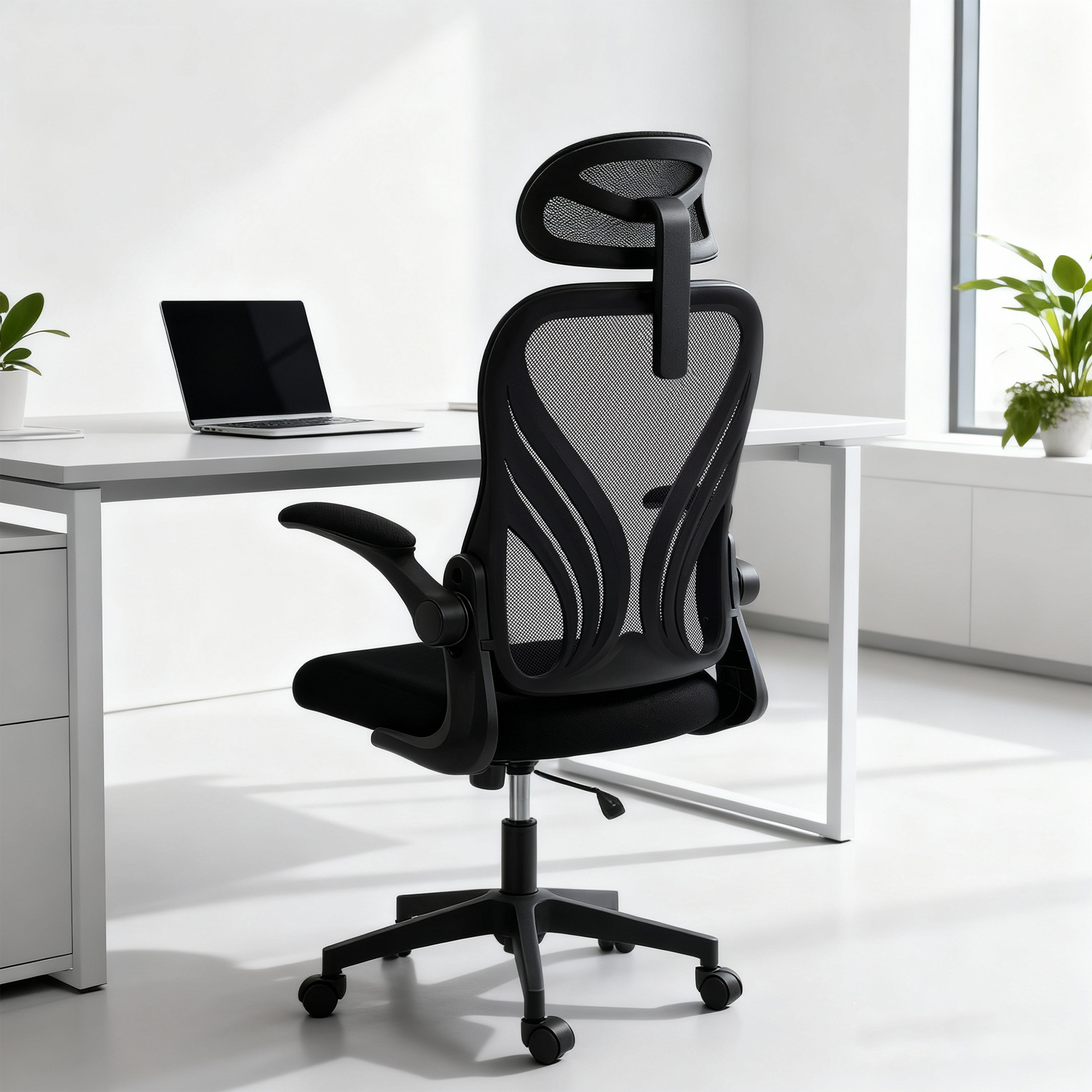 Una sedia da ufficio ergonomica nera davanti a una scrivania bianca con laptop e piante.