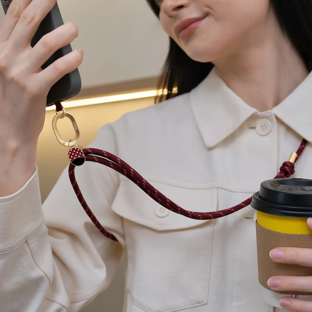 Kobieta w białej bluzce trzyma smartfon i kubek kawy na czerwonym pasku do telefonu.