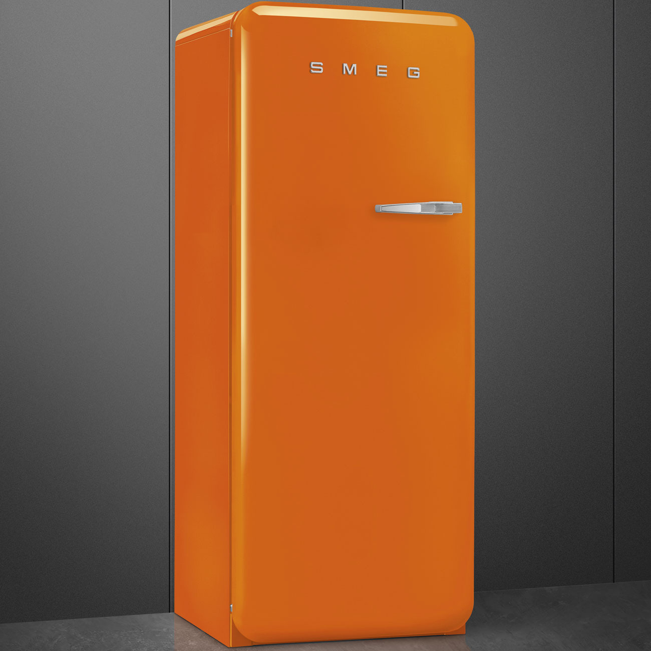 Ein glänzend orangefarbener SMEG-Kühlschrank im Retro-Stil steht vor einer grauen Wand.