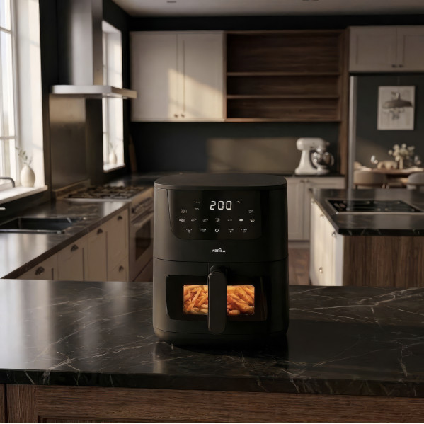 Una friggitrice ad aria nera su un piano di marmo in una cucina moderna, con patatine fritte visibili nella finestra.