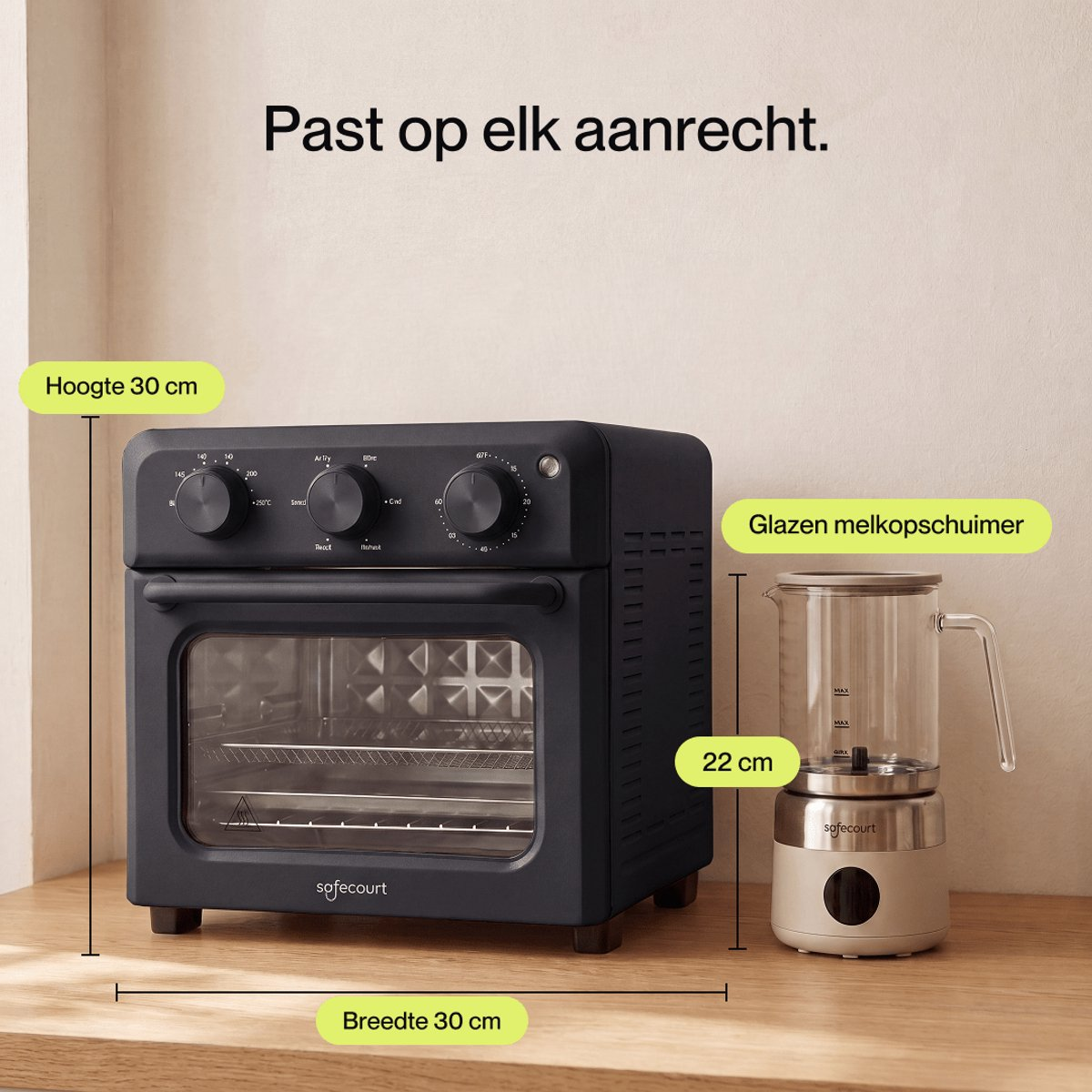 A black countertop oven with three dials and a glass door next to a glass milk frother with a white base.