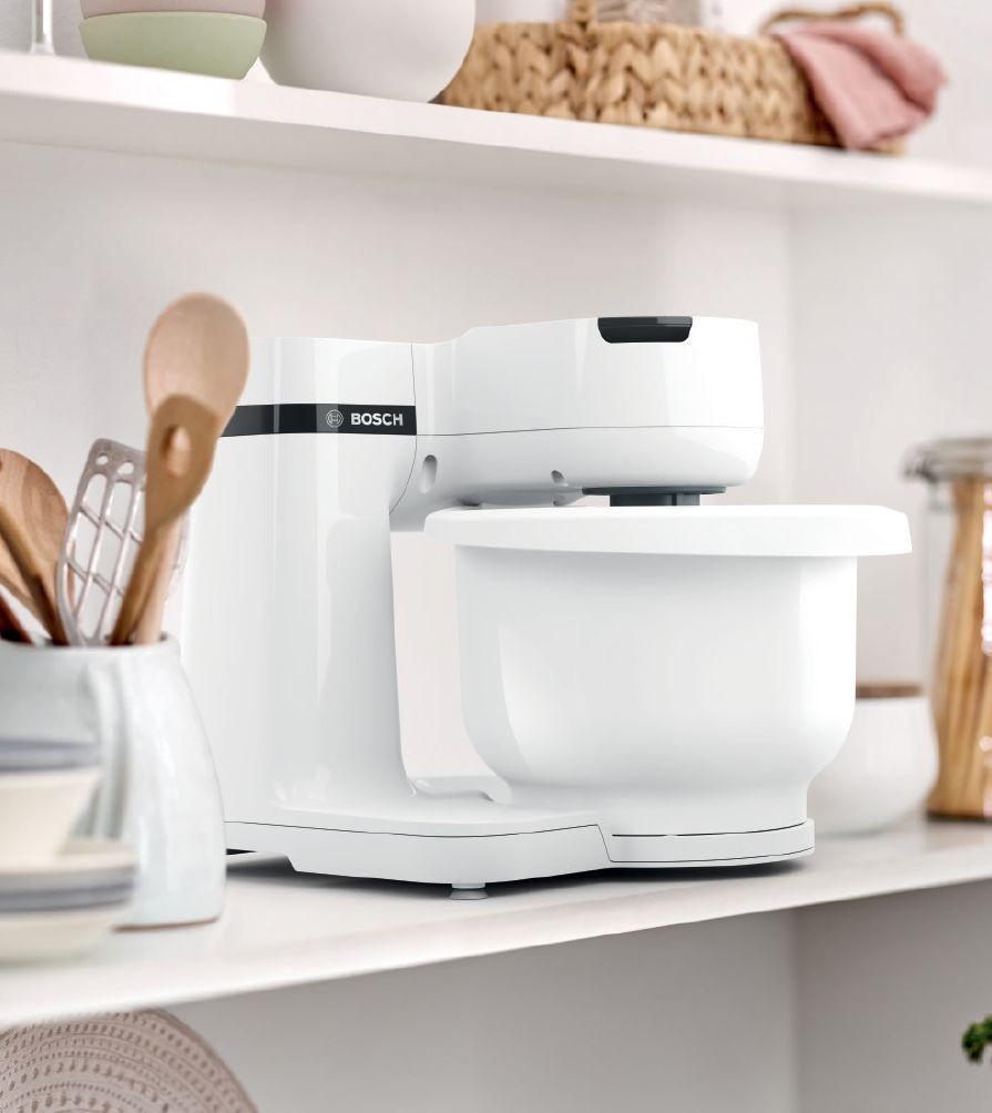 Un robot da cucina Bosch bianco su uno scaffale in una cucina luminosa vicino agli utensili.