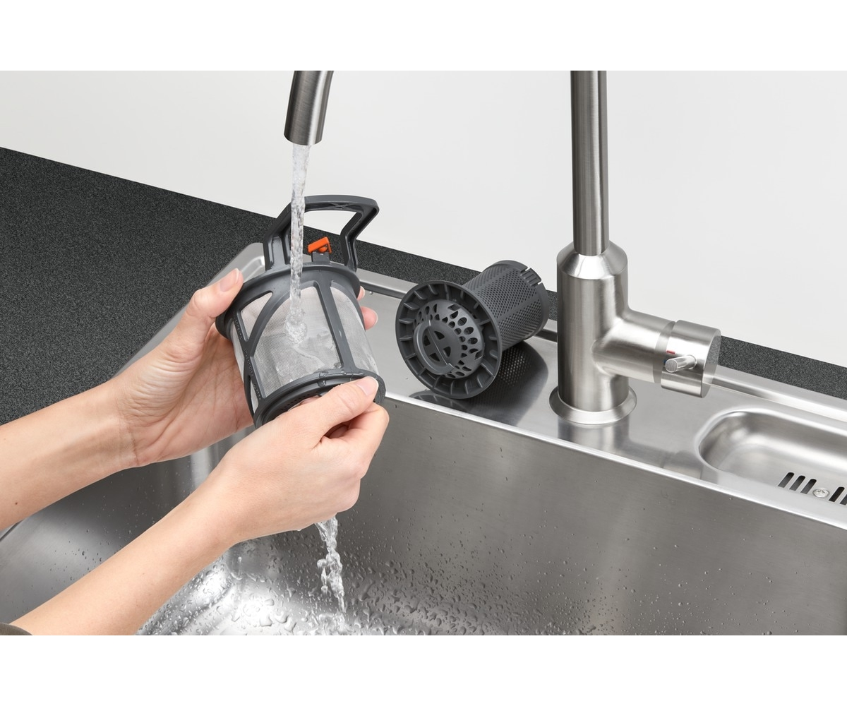 Hände waschen einen grauen Spülmaschinenfilter unter dem Wasserhahn in einem Edelstahlbecken.