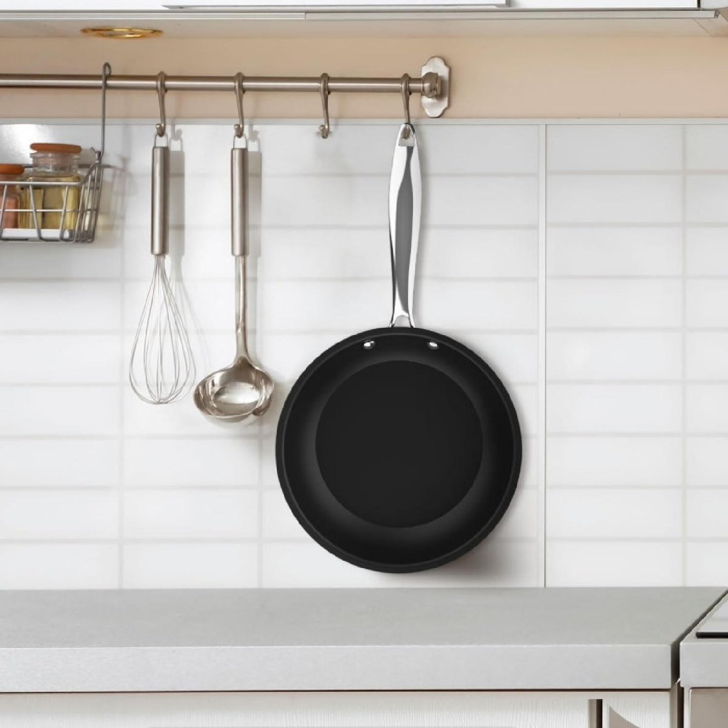 Una sartén negra, un batidor y un cucharón cuelgan de un riel metálico en una pared de cocina.