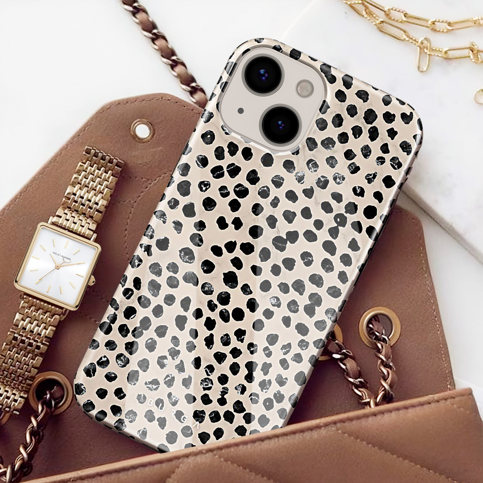Ein Smartphone mit Dalmatiner-Muster liegt auf einer braunen Ledertasche neben einer GoldUhr.