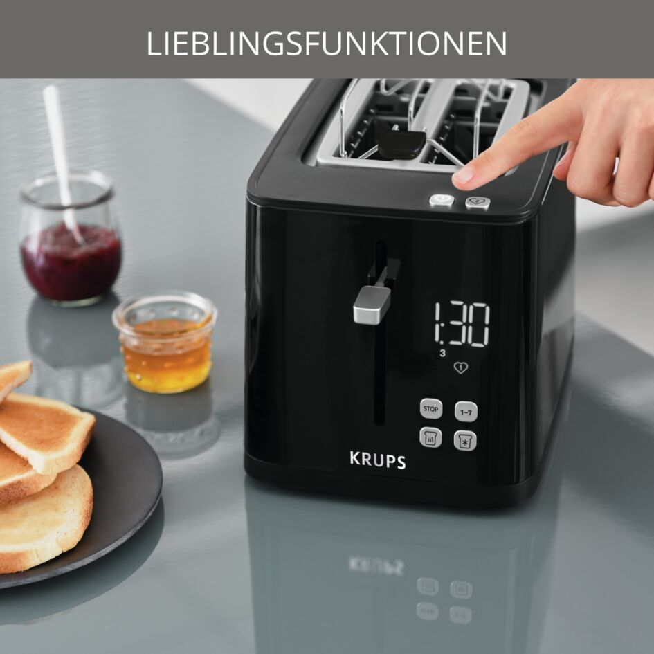 Hand drückt Knopf auf schwarzem Krups-Toaster mit digitaler Anzeige, daneben Toast und Gläser mit Aufstrich.