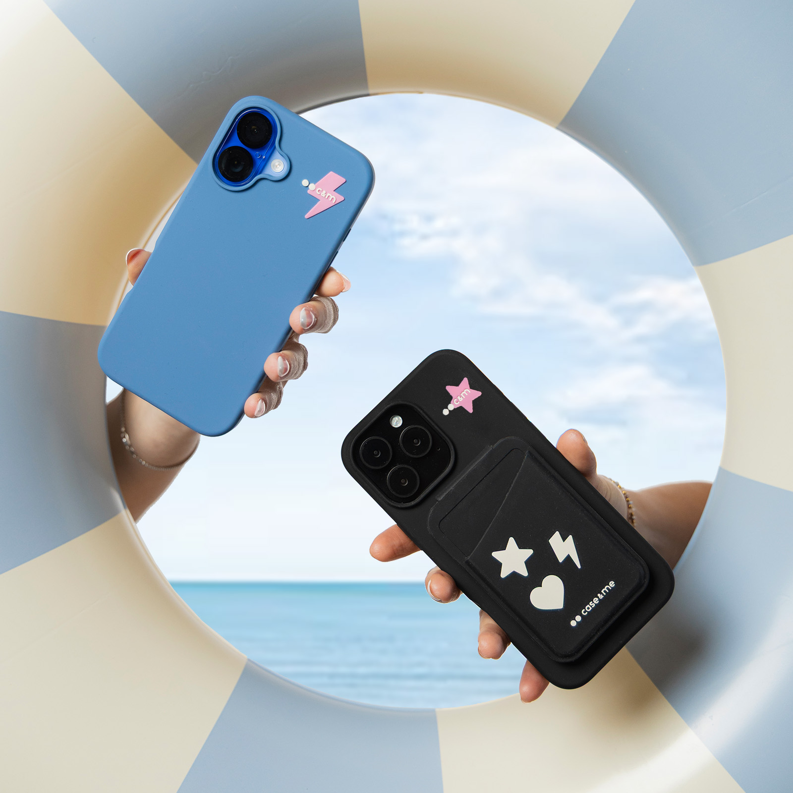 Dos manos sostienen teléfonos azules y negros con pegatinas ante un flotador azul y blanco y el mar.