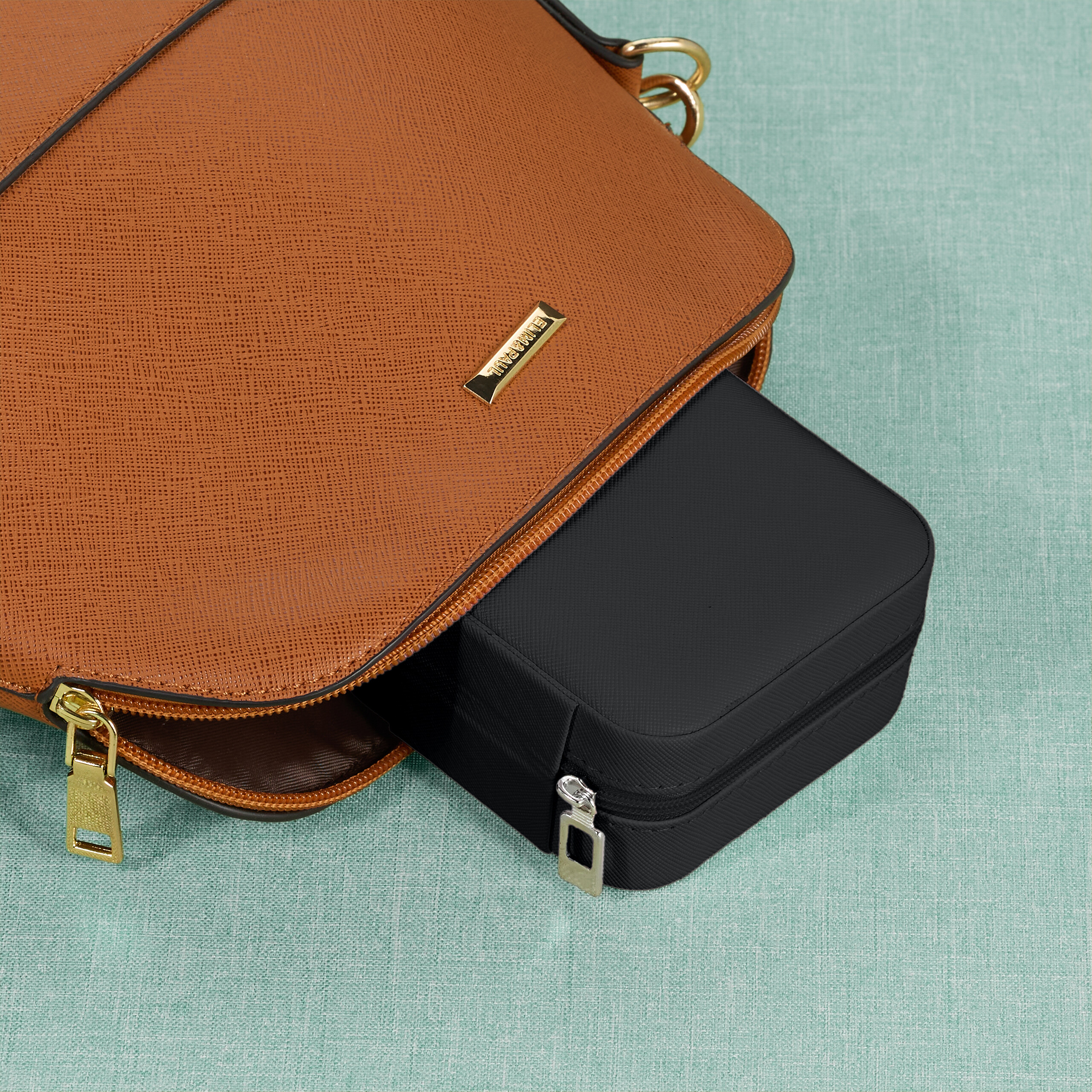 Eine kleine schwarze Tasche liegt teilweise in einer größeren braunen Handtasche auf grünem Untergrund.