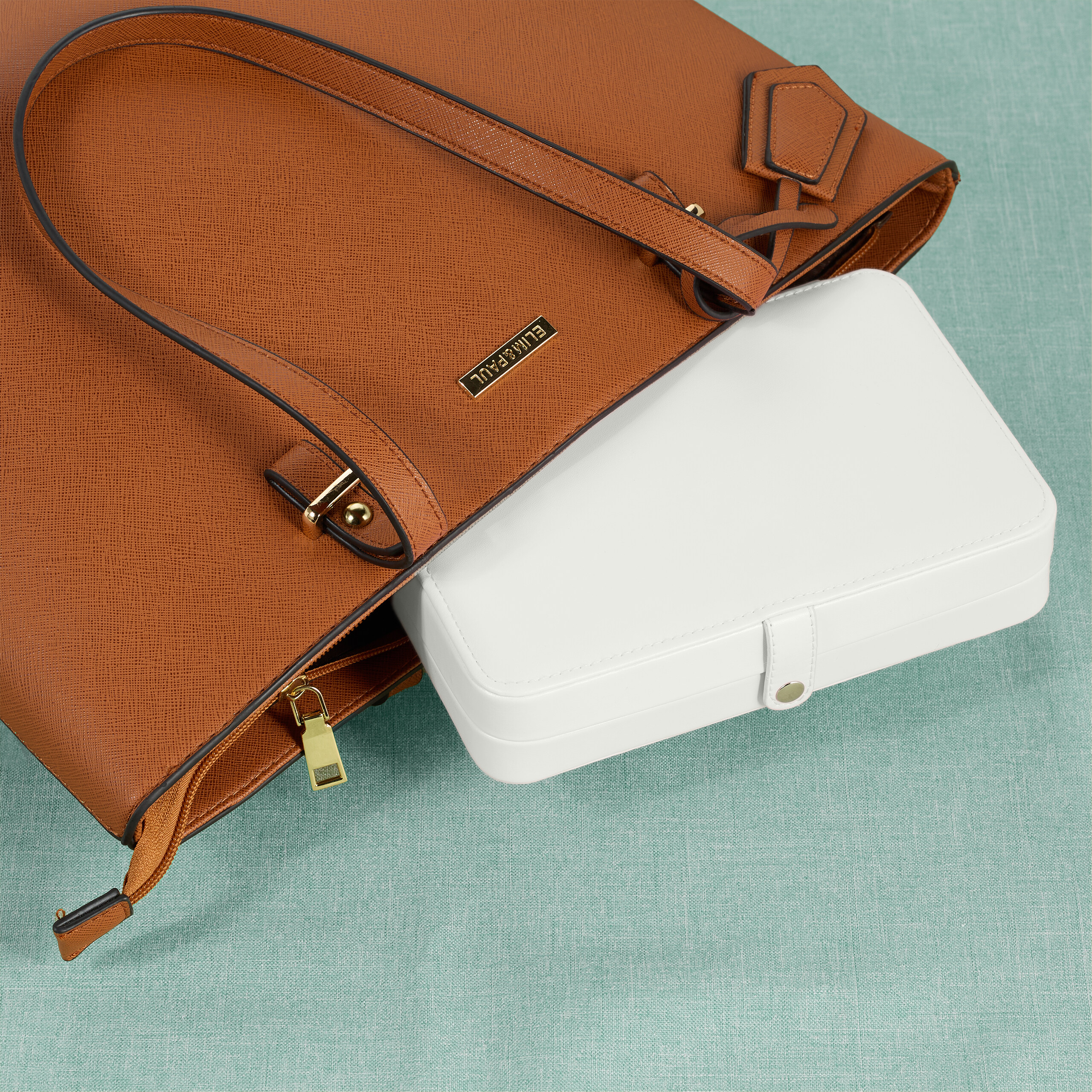 Eine braune Handtasche mit einer weißen Schachtel innen auf einer türkisen Unterlage.
