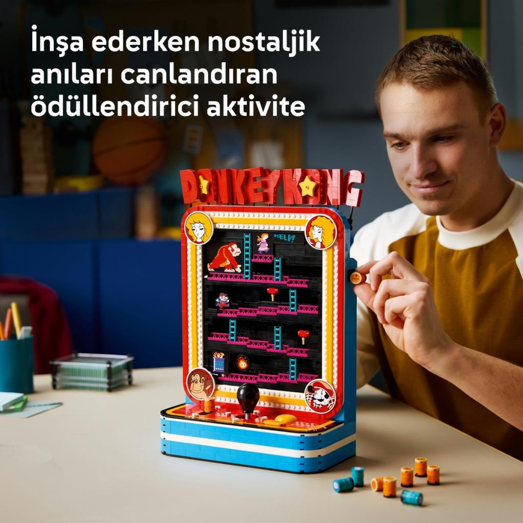 Bir adam masada renkli bir LEGO Donkey Kong atari oyunu modeli inşa ediyor.