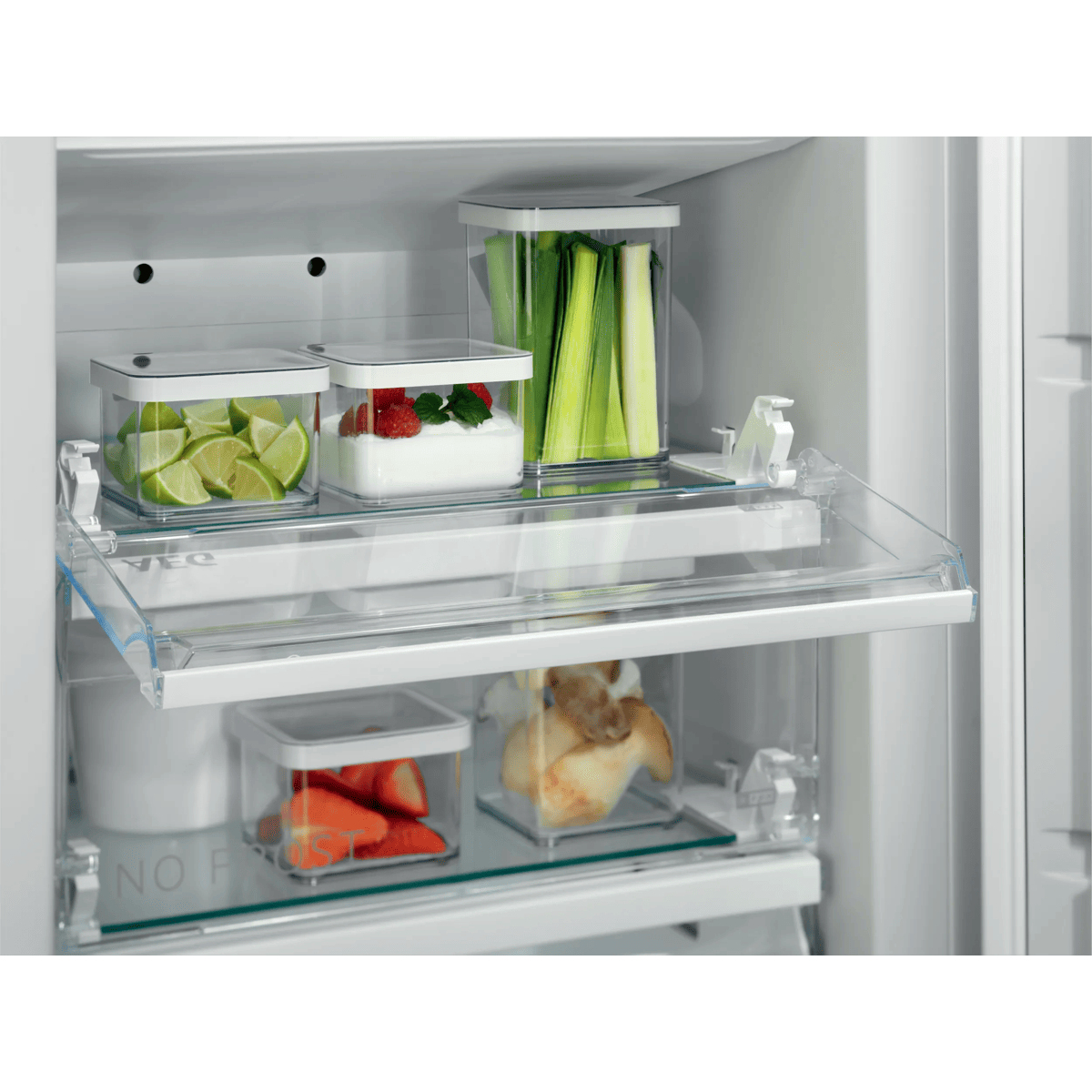Interno di un frigorifero con ripiani in vetro e contenitori organizzati con lime, fragole, porri e dolci.