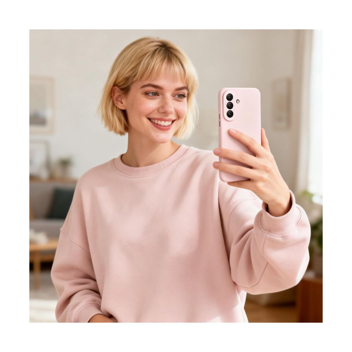 Eine blonde Frau in einem rosa Sweatshirt lächelt, während sie ein Selfie mit einem rosa Handy macht.